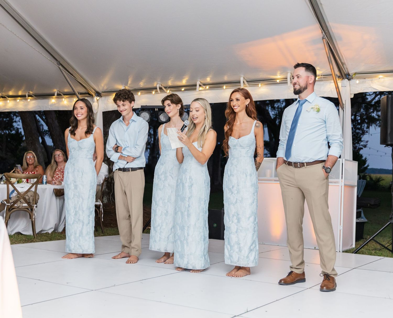 Wedding party dancing together on white dance floor at outdoor reception during sunset celebration.