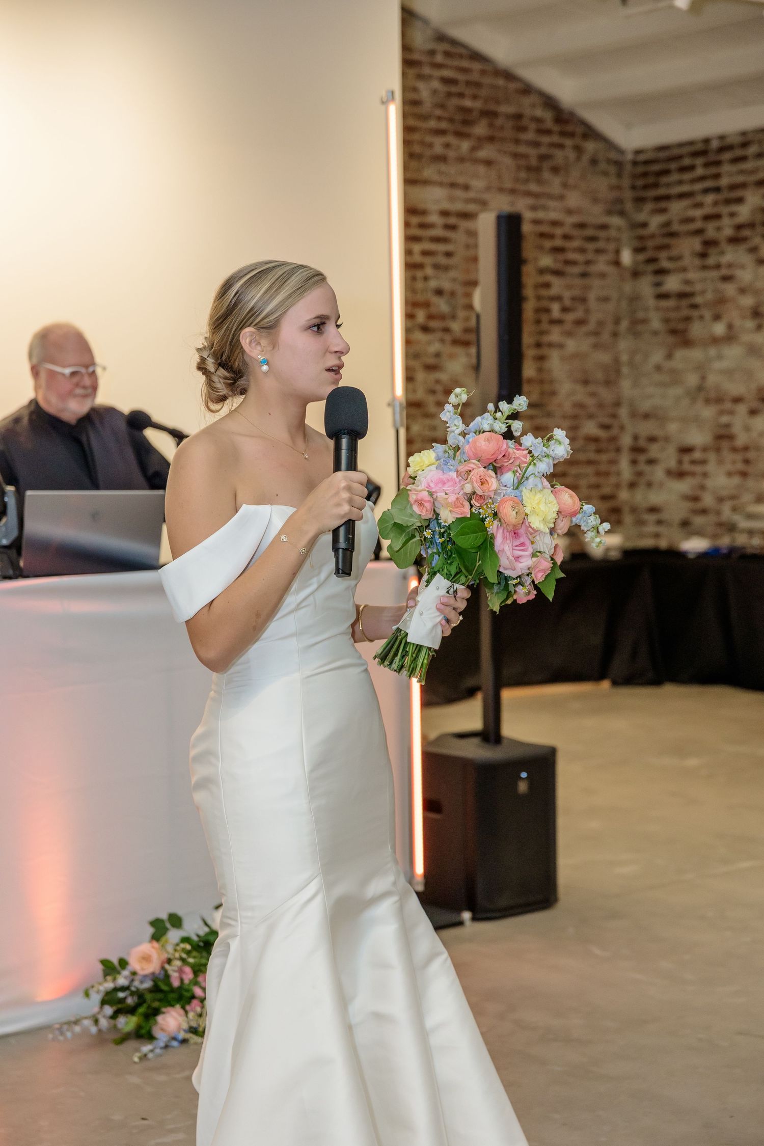 Wedding party dancing in a rustic brick-walled venue with exposed ceiling beams.