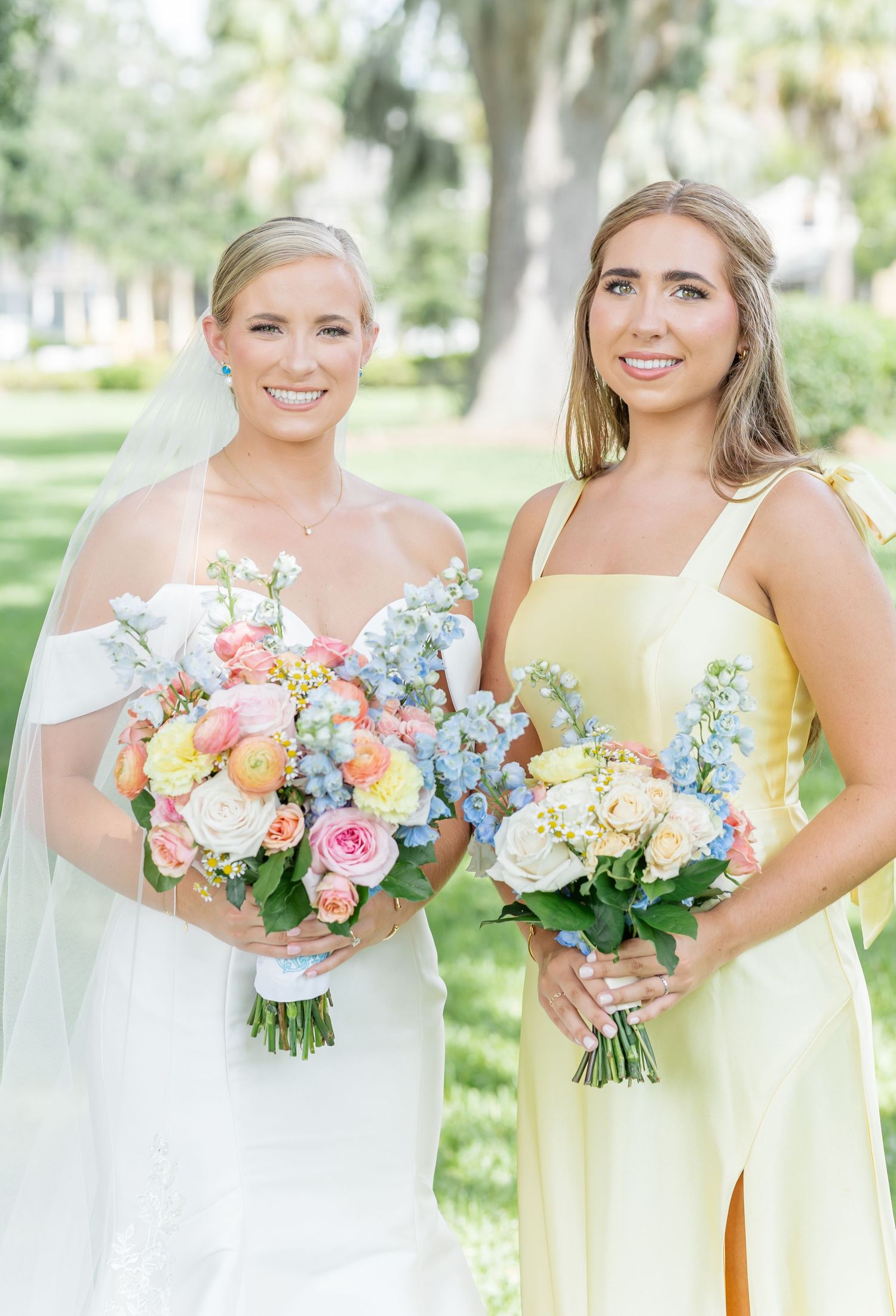 Bridesmaids in yellow dresses and bride in white hold colorful spring bouquets featuring pink, peach and blue flowers.
