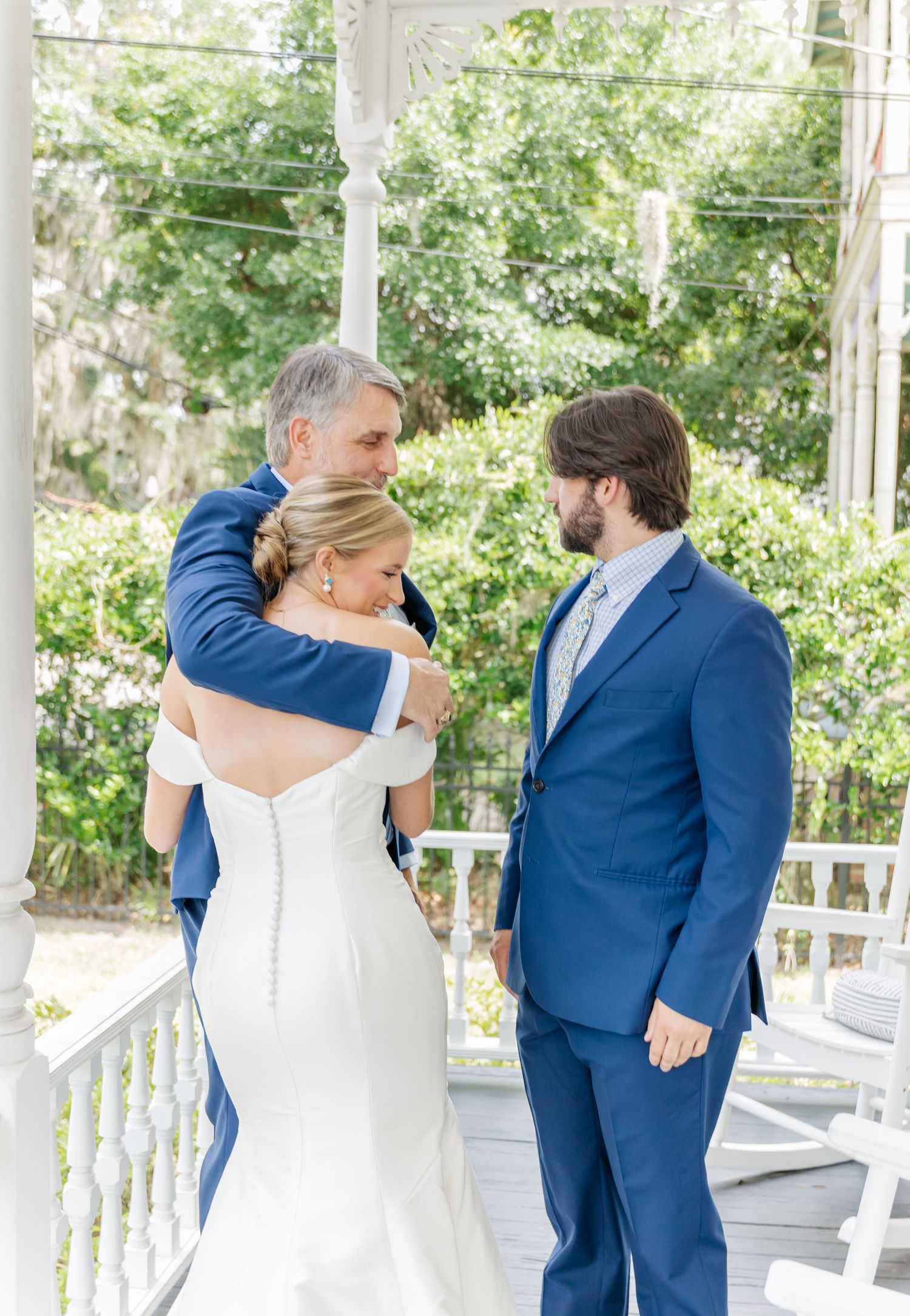 An intimate wedding ceremony moment on a white porch surrounded by lush greenery on a bright sunny day.