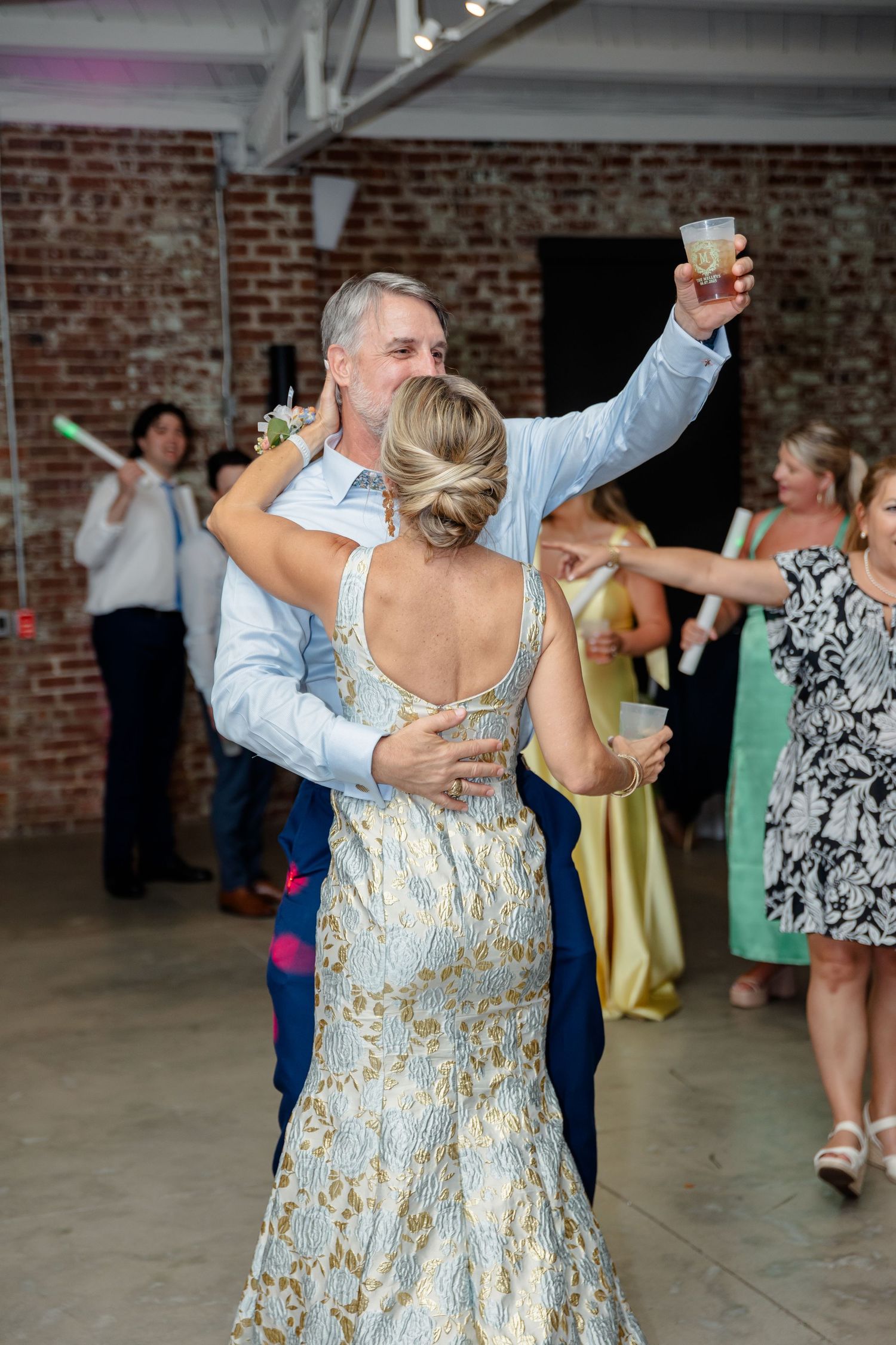 A couple dances together at a wedding reception in an industrial brick venue with guests in the background.