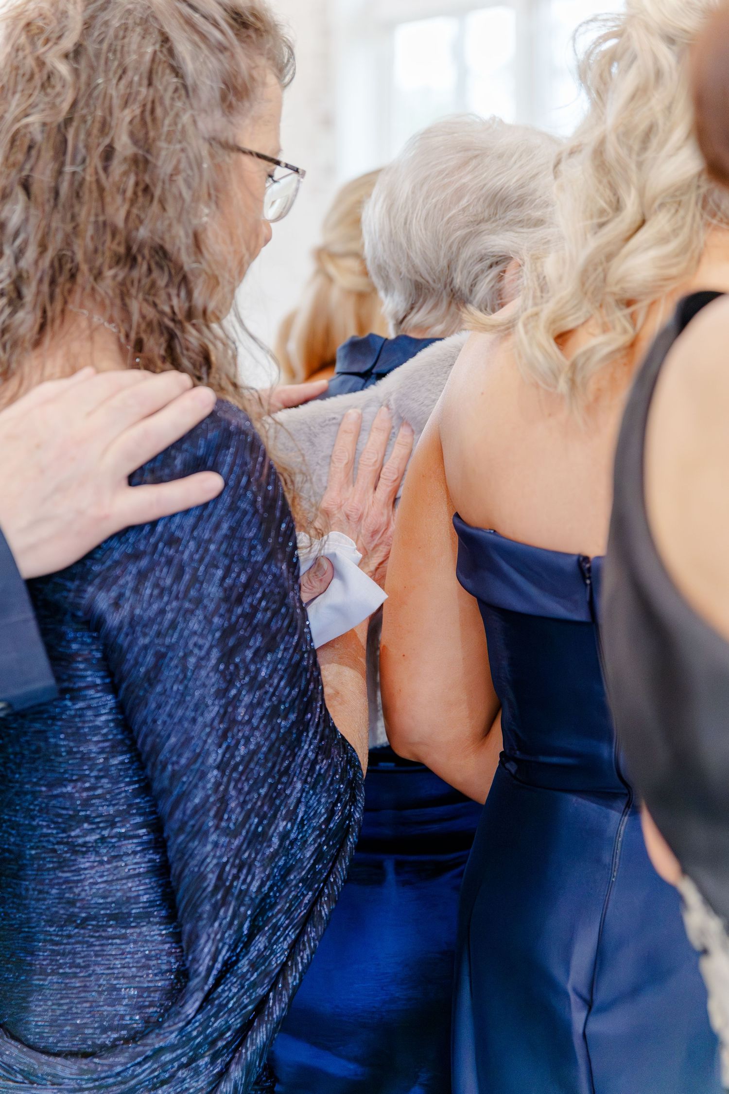 Wedding guests in blue formal attire share an emotional moment, with hands resting on shoulders in support.