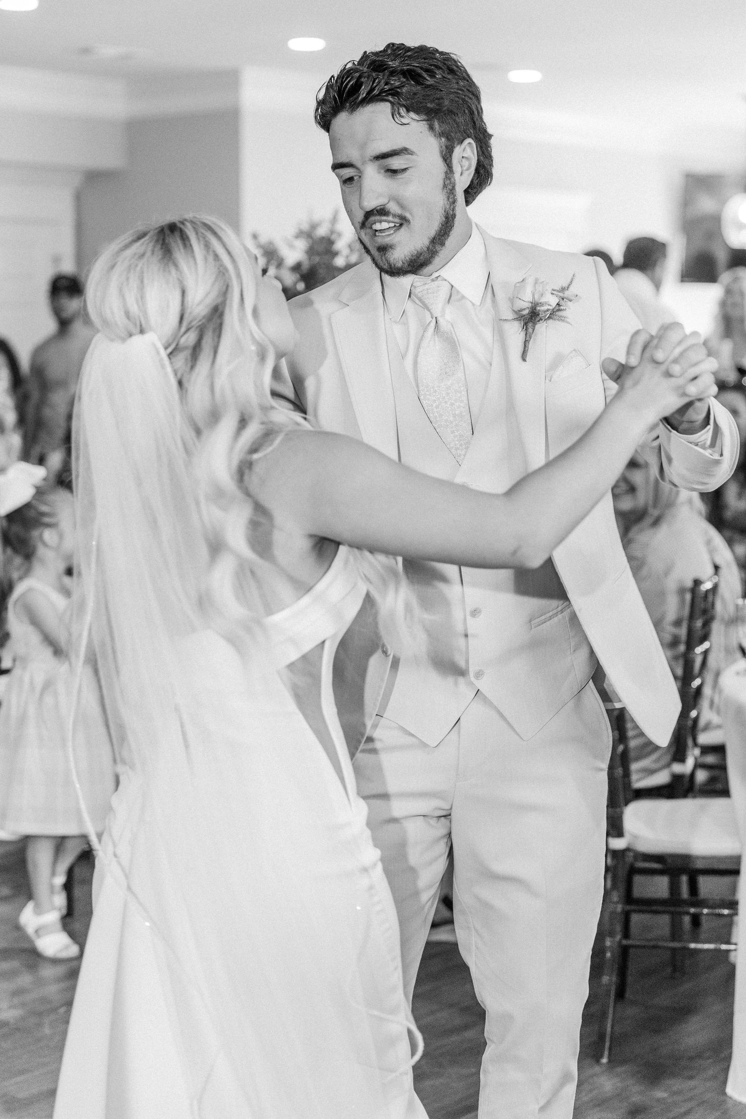 Black and white photo of bride and groom sharing first dance, groom smiling warmly at his bride.