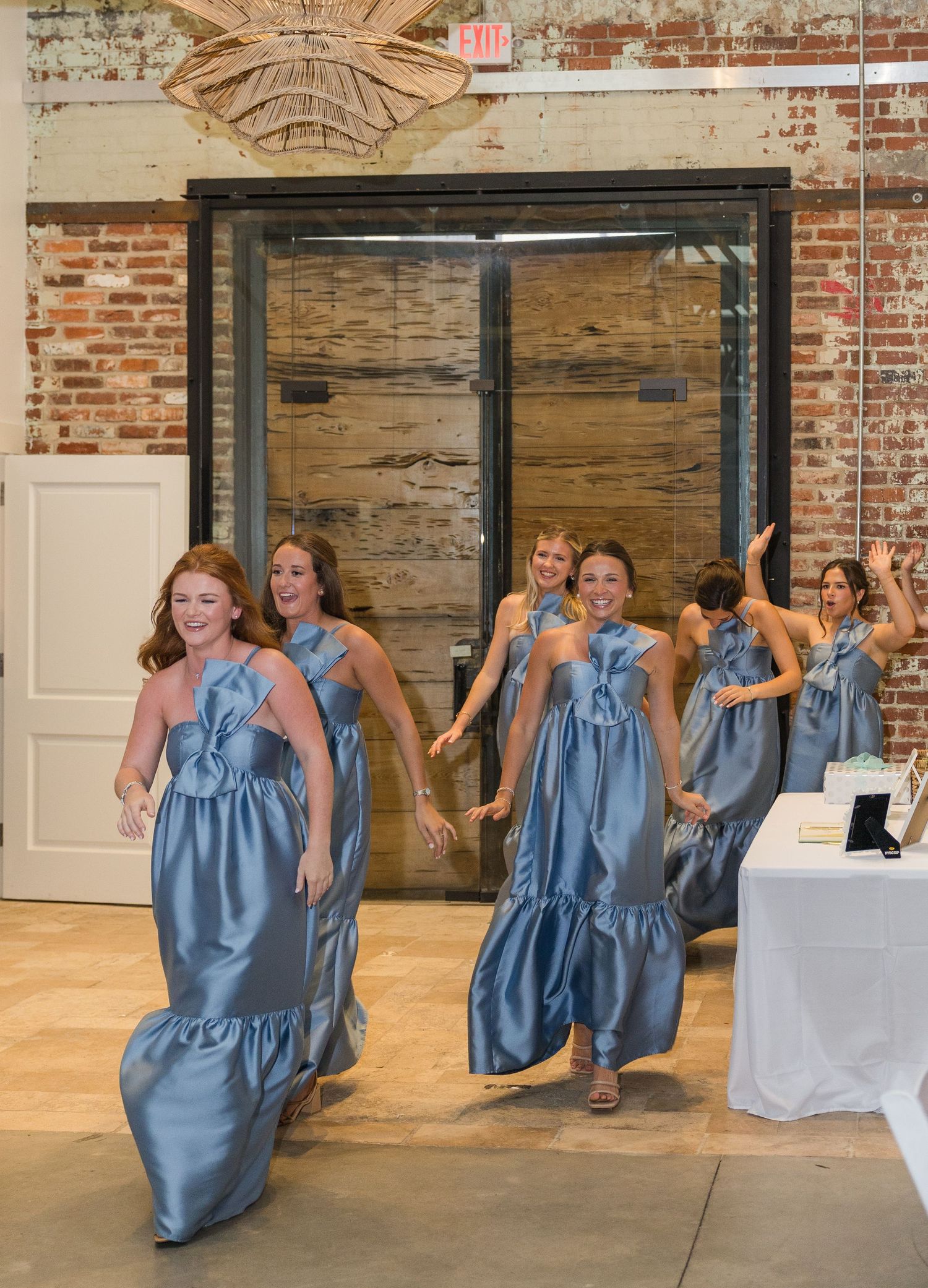 Bridesmaids in blue satin gowns make a joyful entrance running into the wedding reception venue.