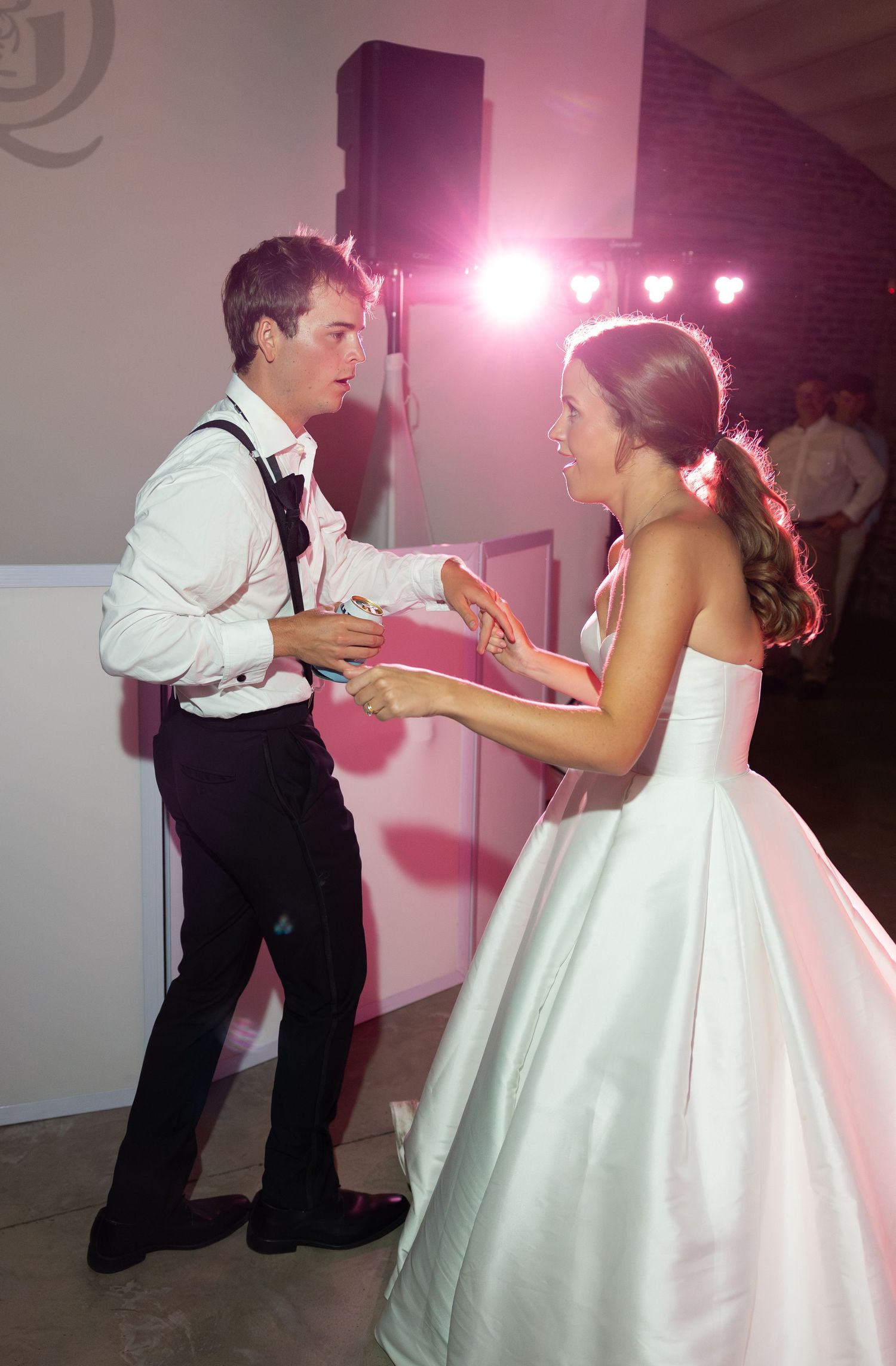 Bride and groom share a fun dance together under pink reception lighting at their wedding celebration.