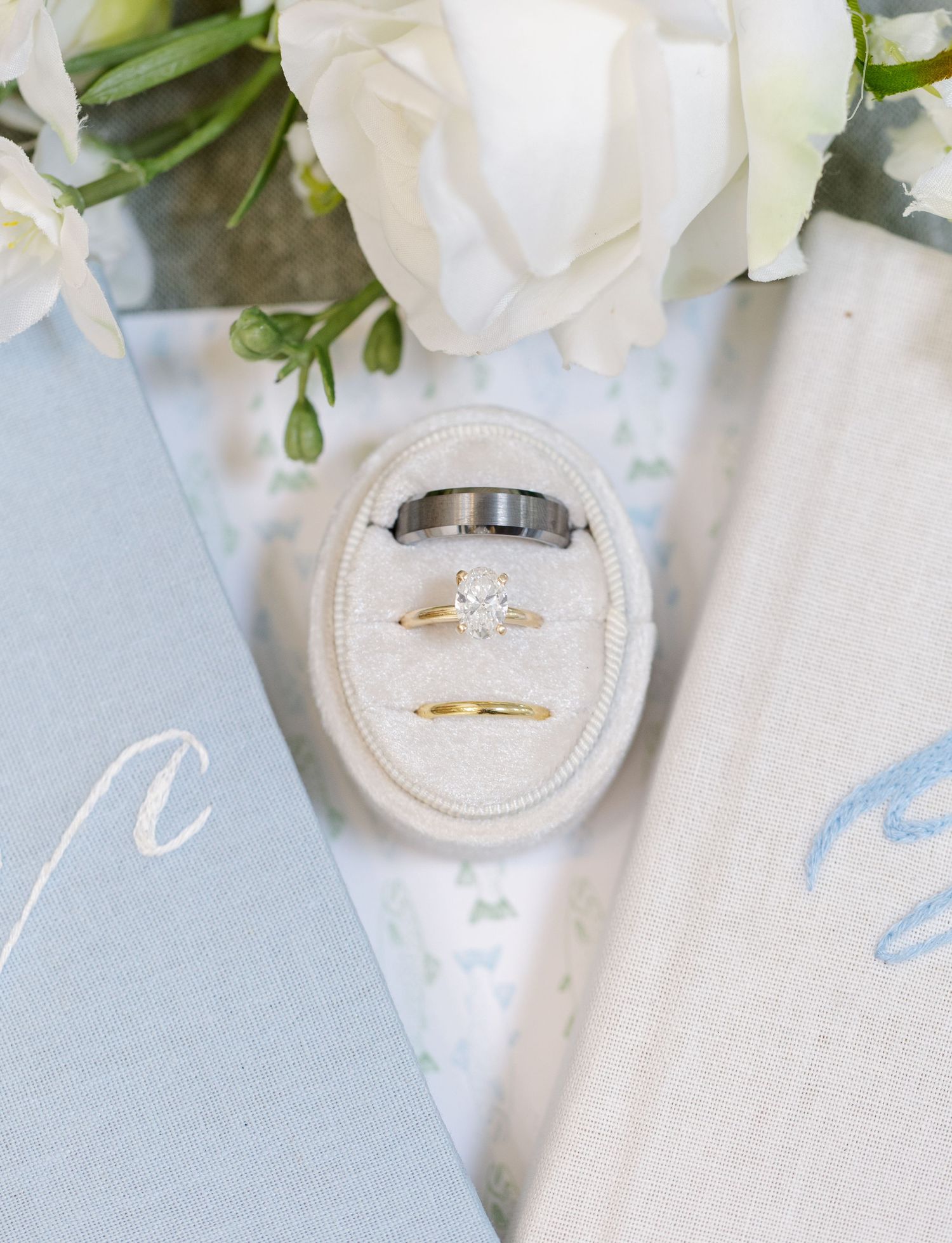 Three wedding rings displayed in a velvet ring box with white roses and blue stationery.