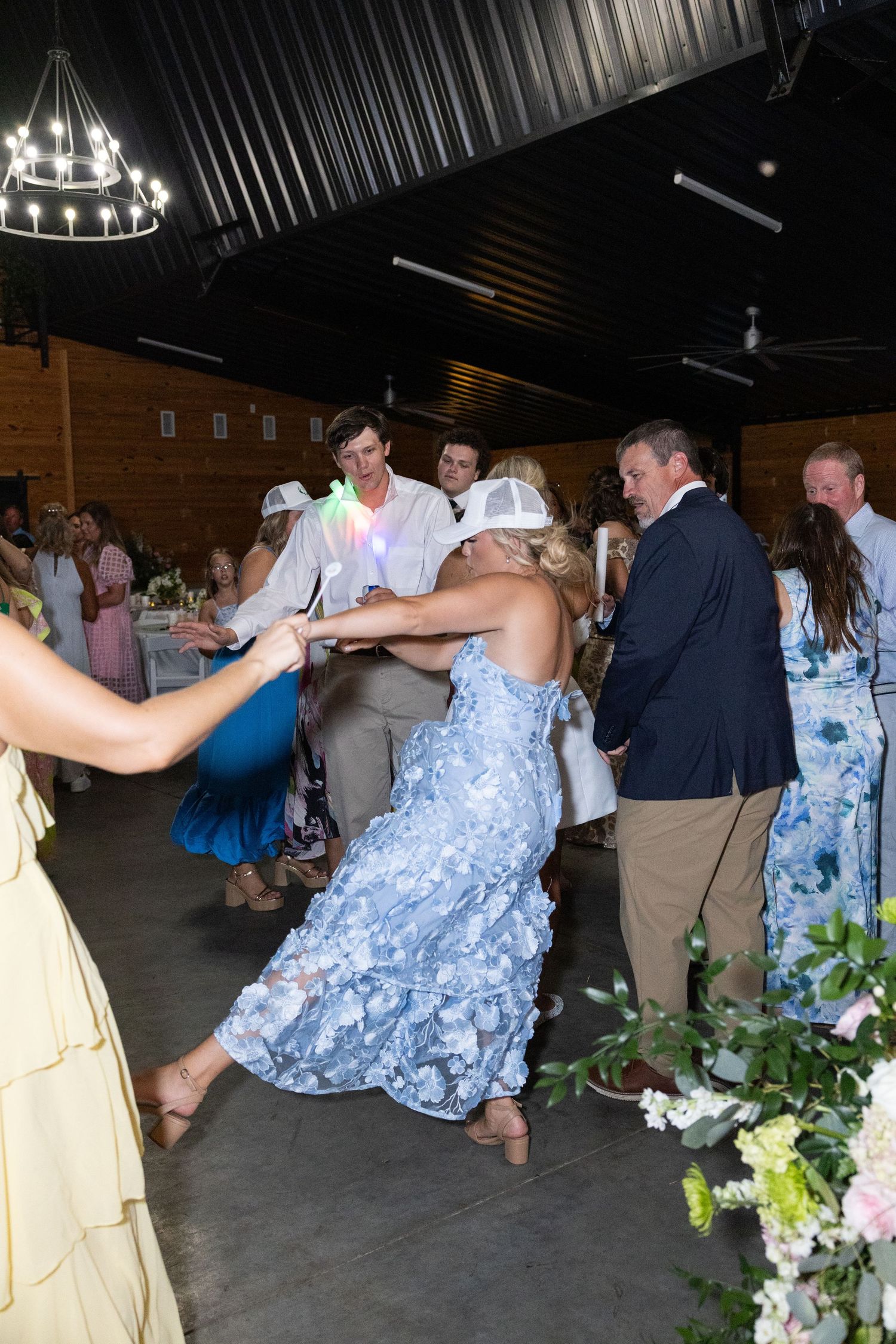 Wedding guest in blue floral dress dancing energetically at rustic barn reception venue.