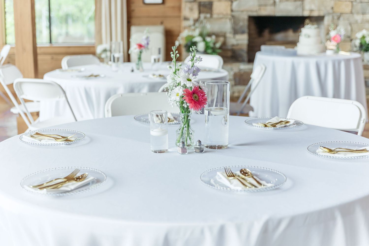 Round wedding reception table with white linens, gold flatware, and pink floral centerpiece.