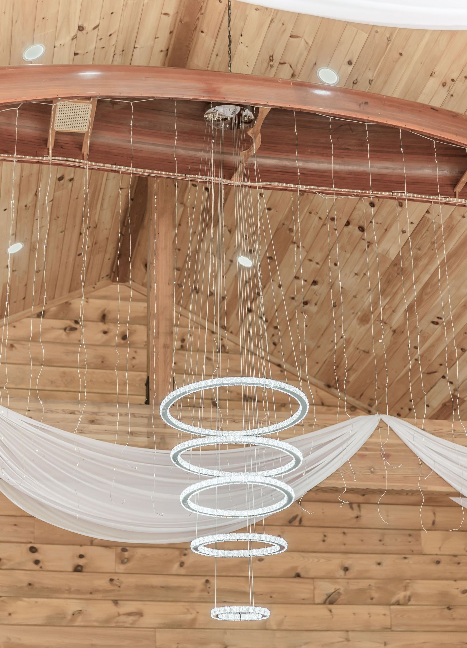 Modern circular LED chandeliers with draped white fabric in wooden ceiling venue.