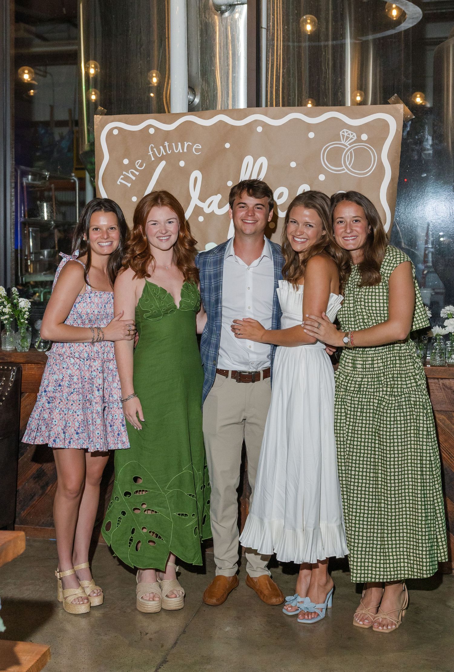 Five young guests pose smiling before a future Walkers wedding engagement party banner.