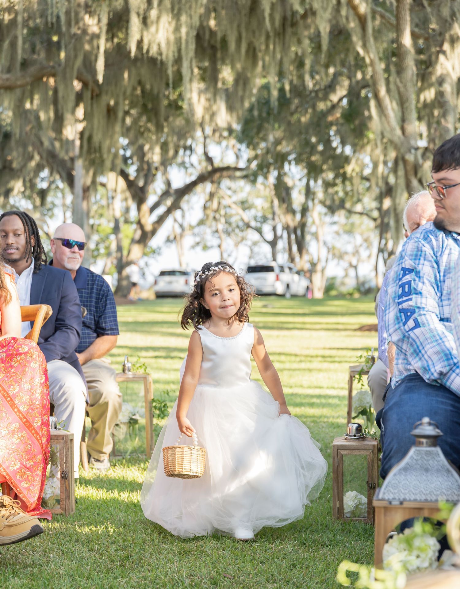 Outdoor wedding ceremony under Spanish moss draped trees with guests seated on wooden chairs.