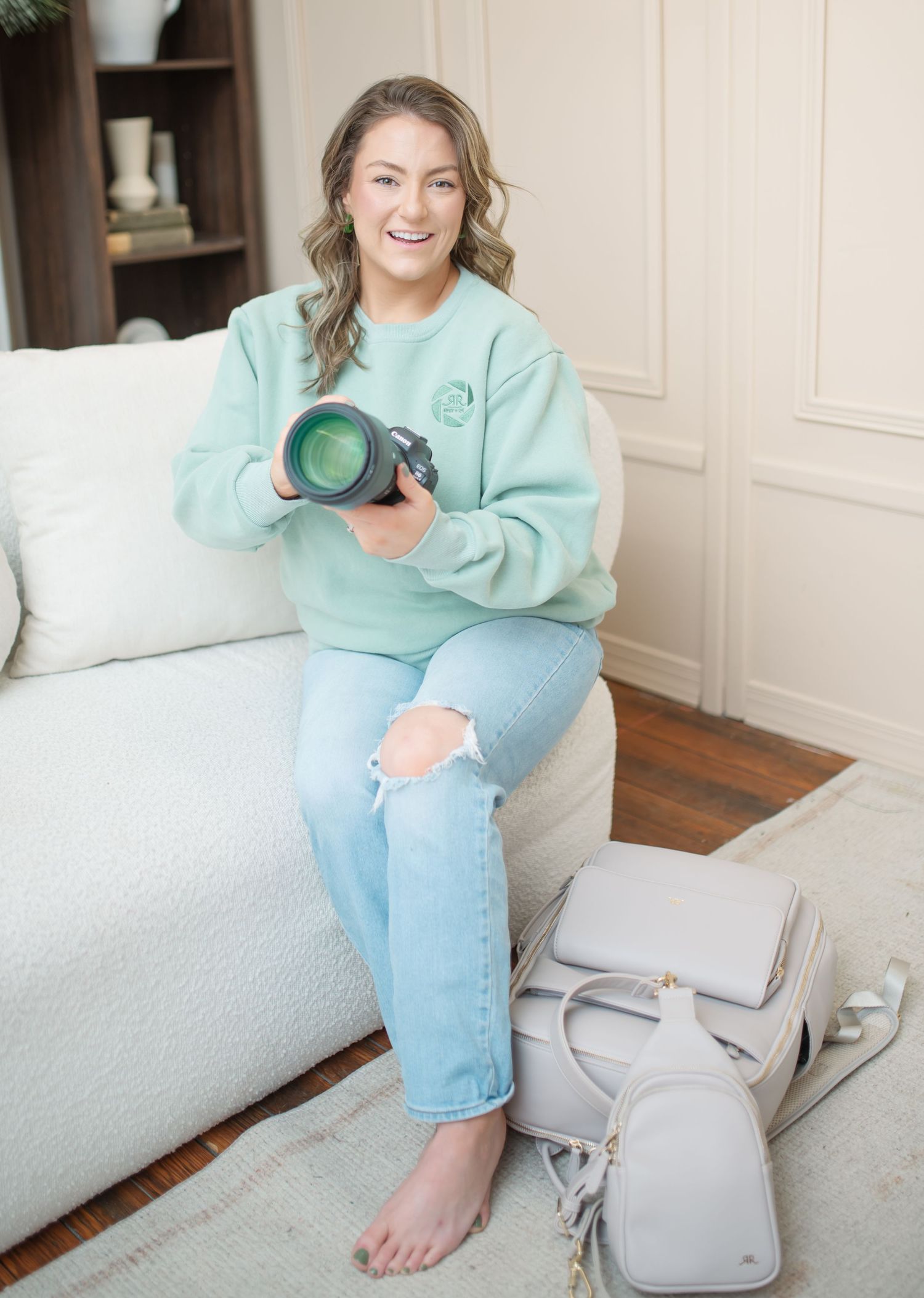 A person in a mint green sweater and light jeans sits casually on a white couch with a gray backpack nearby.