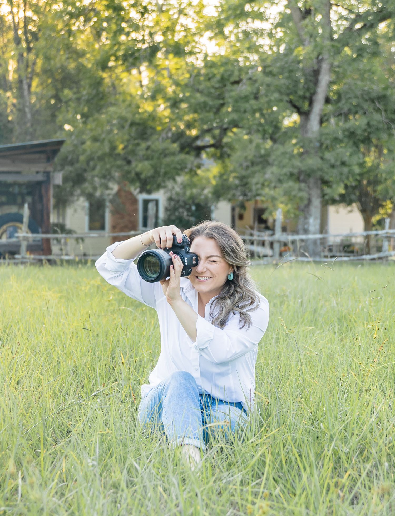 A photographer lies in a grassy meadow taking creative shots during golden hour with a professional camera.