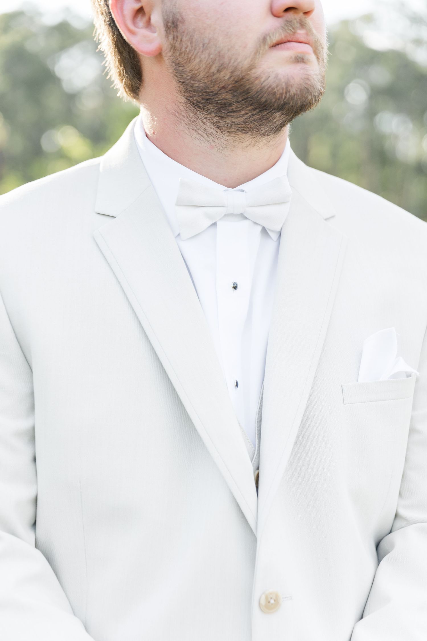 Close-up detail of groom's classic white tuxedo with bow tie and pocket square.