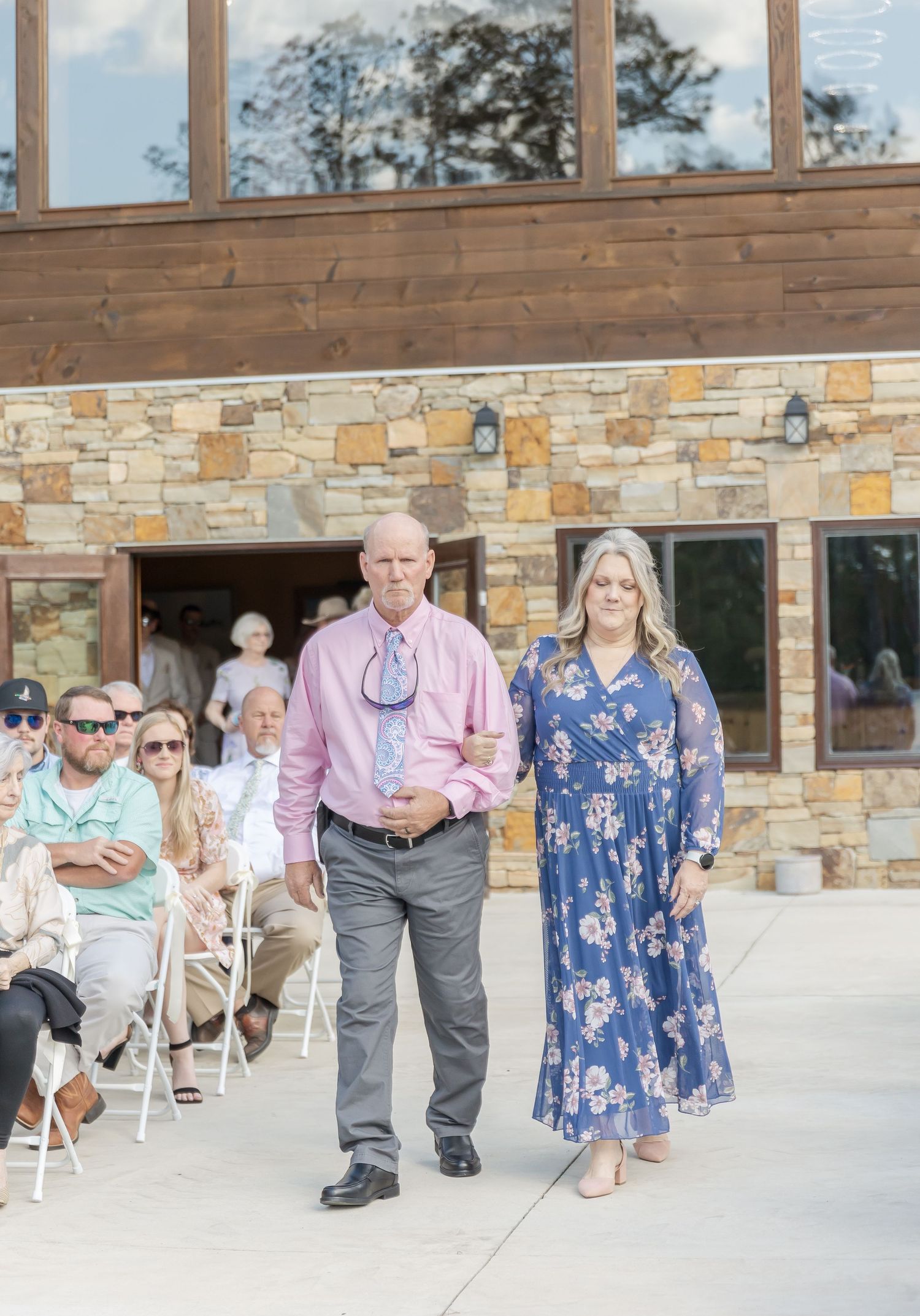 Formal procession outside stone and wood wedding venue with seated guests.