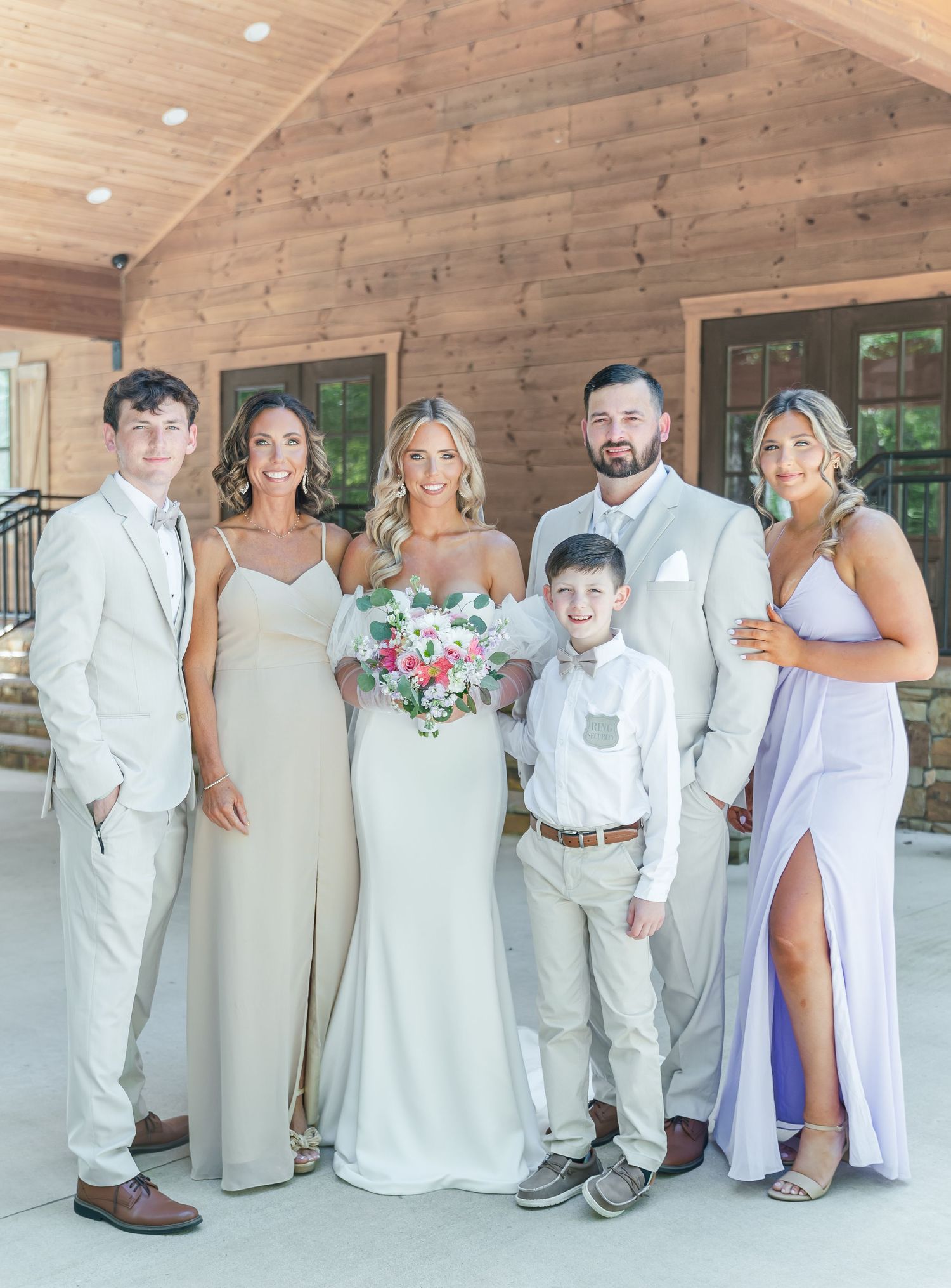 Wedding party in coordinated white and lavender attire poses at rustic venue.