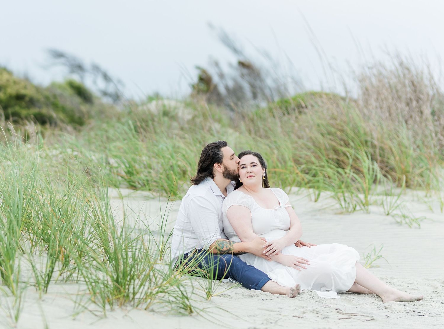 Couple sharing an intimate moment among beach grass dunes.