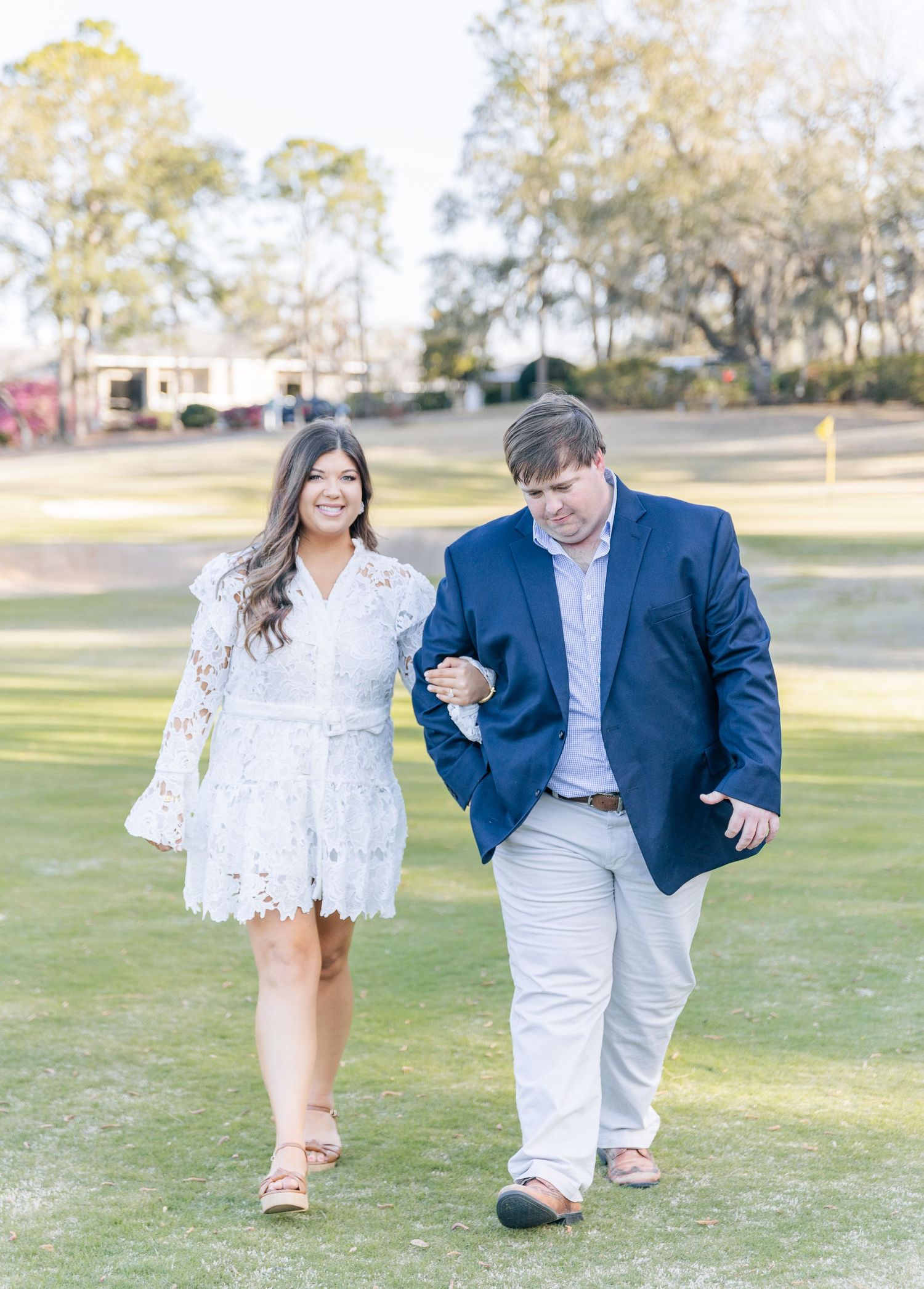 Happy couple walking on a grassy lawn with Spanish moss trees in the background.