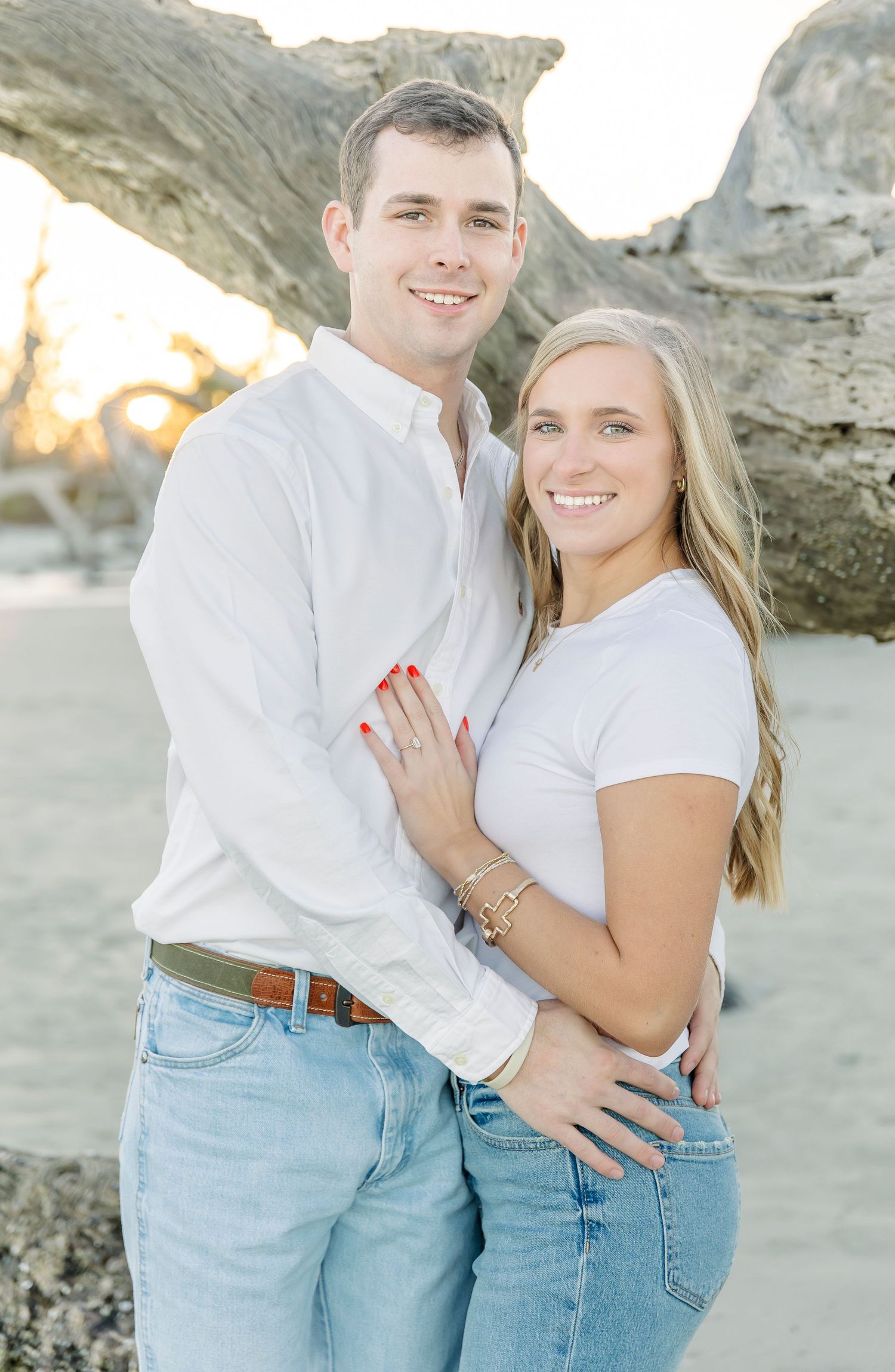 Happy couple in casual white and denim outfits posing together on beach at sunset.
