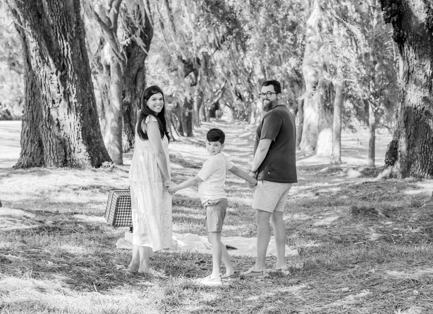 A family holds hands while standing in a dreamy black and white forest scene.