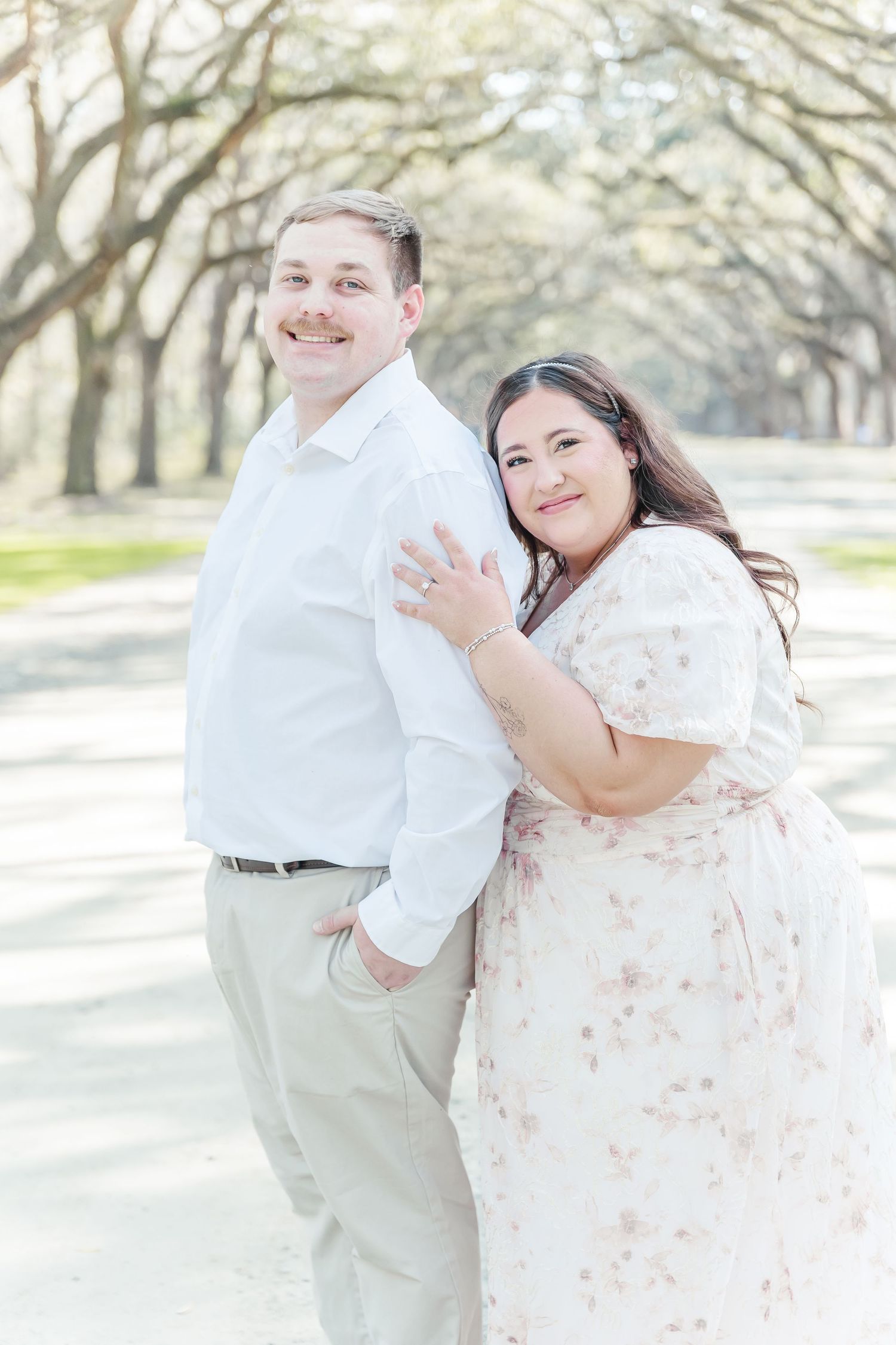 Happy couple posing casually on a scenic oak-lined pathway during their engagement shoot.