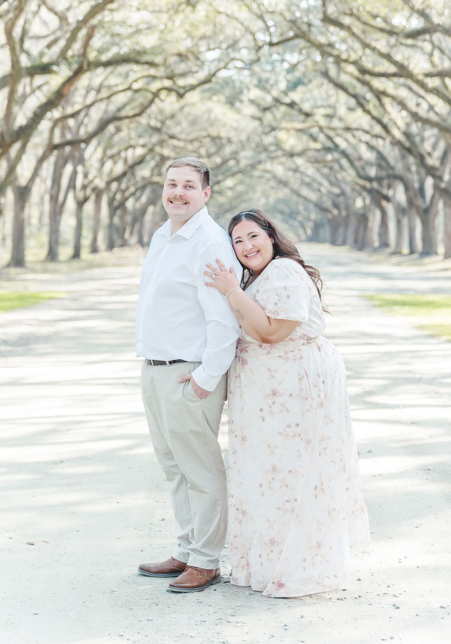 A happy couple poses together on a tree-lined path in spring.