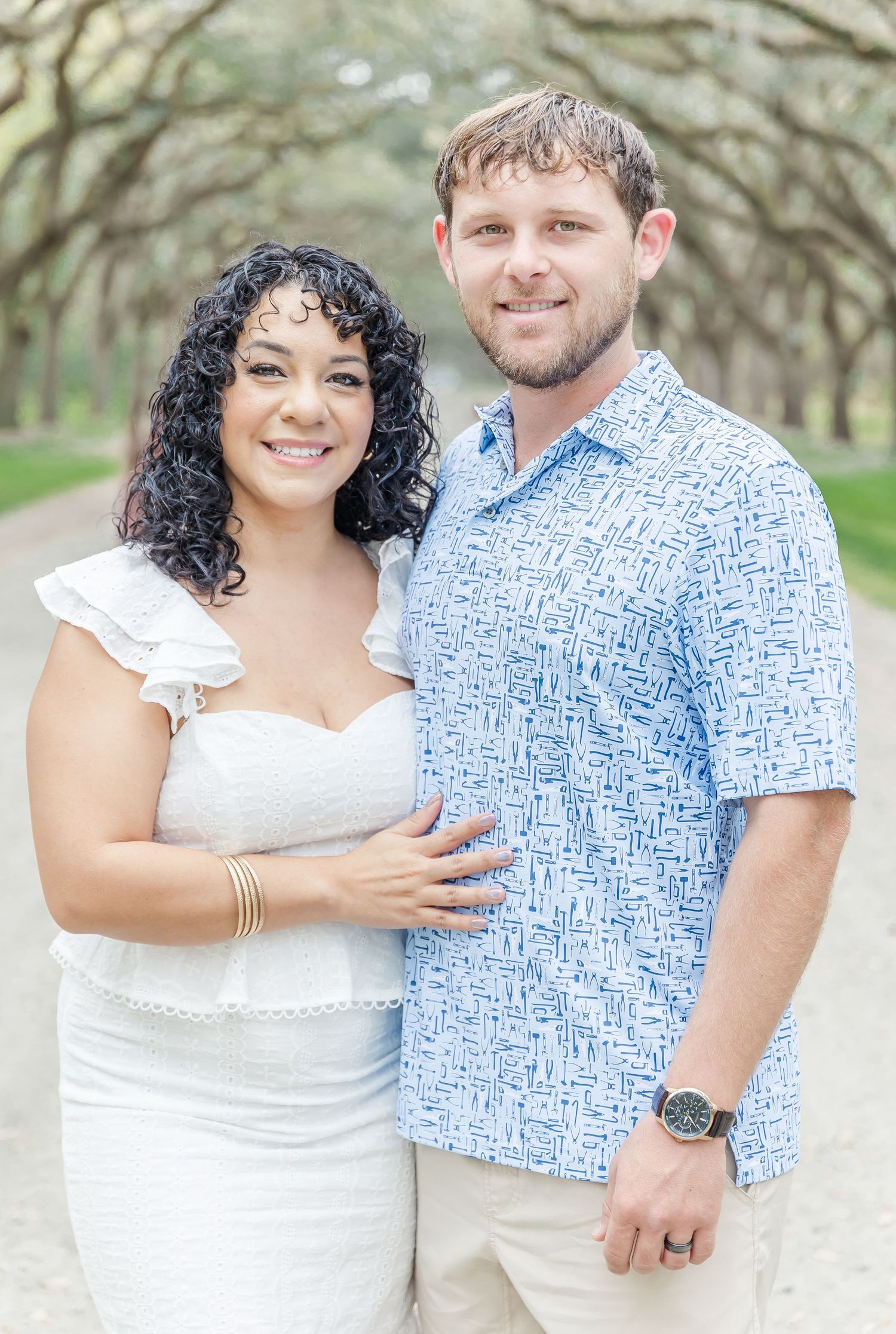 Couple in white and blue outfits pose for portrait under oak trees.