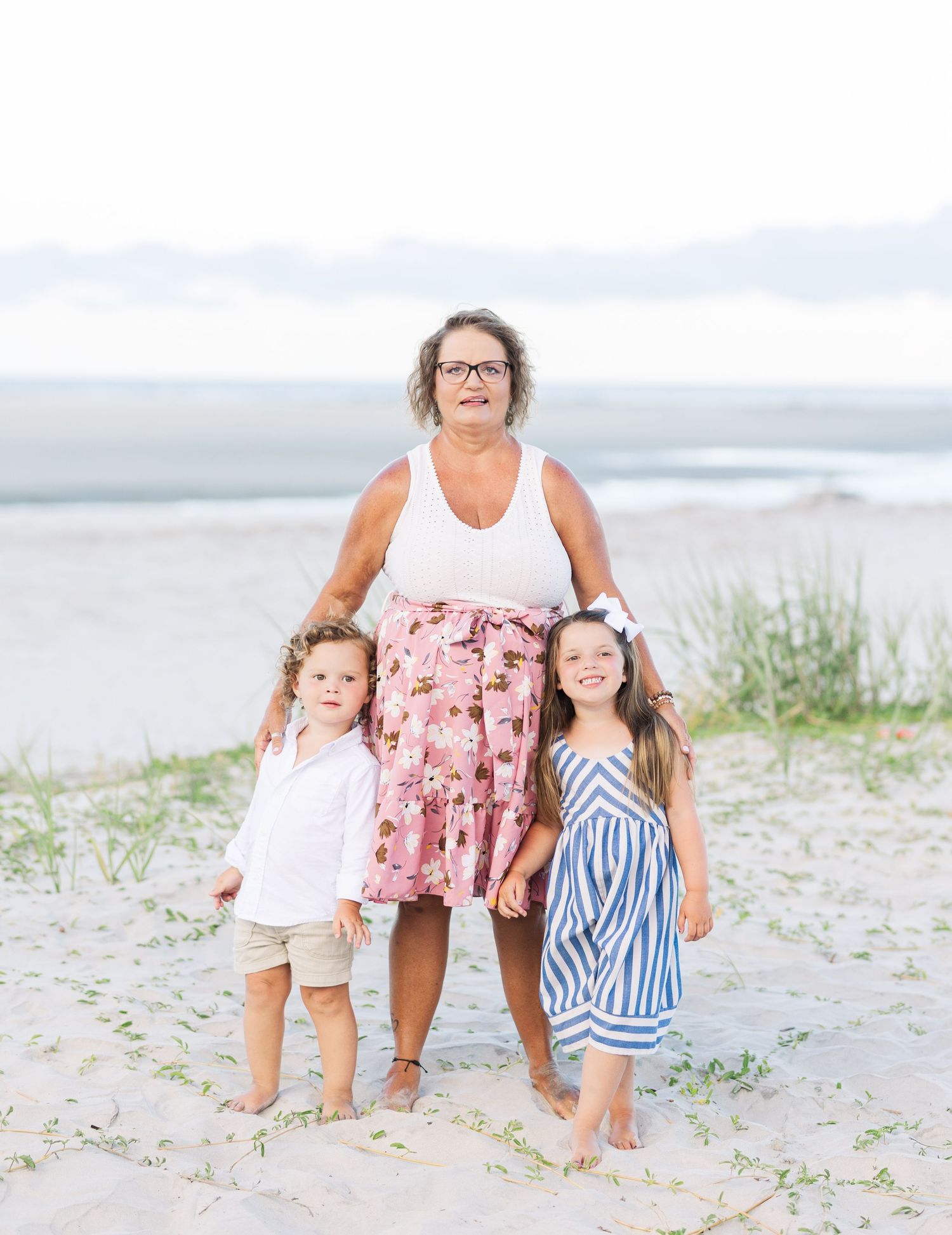 Three people pose together on a beach with dunes and ocean in the background.