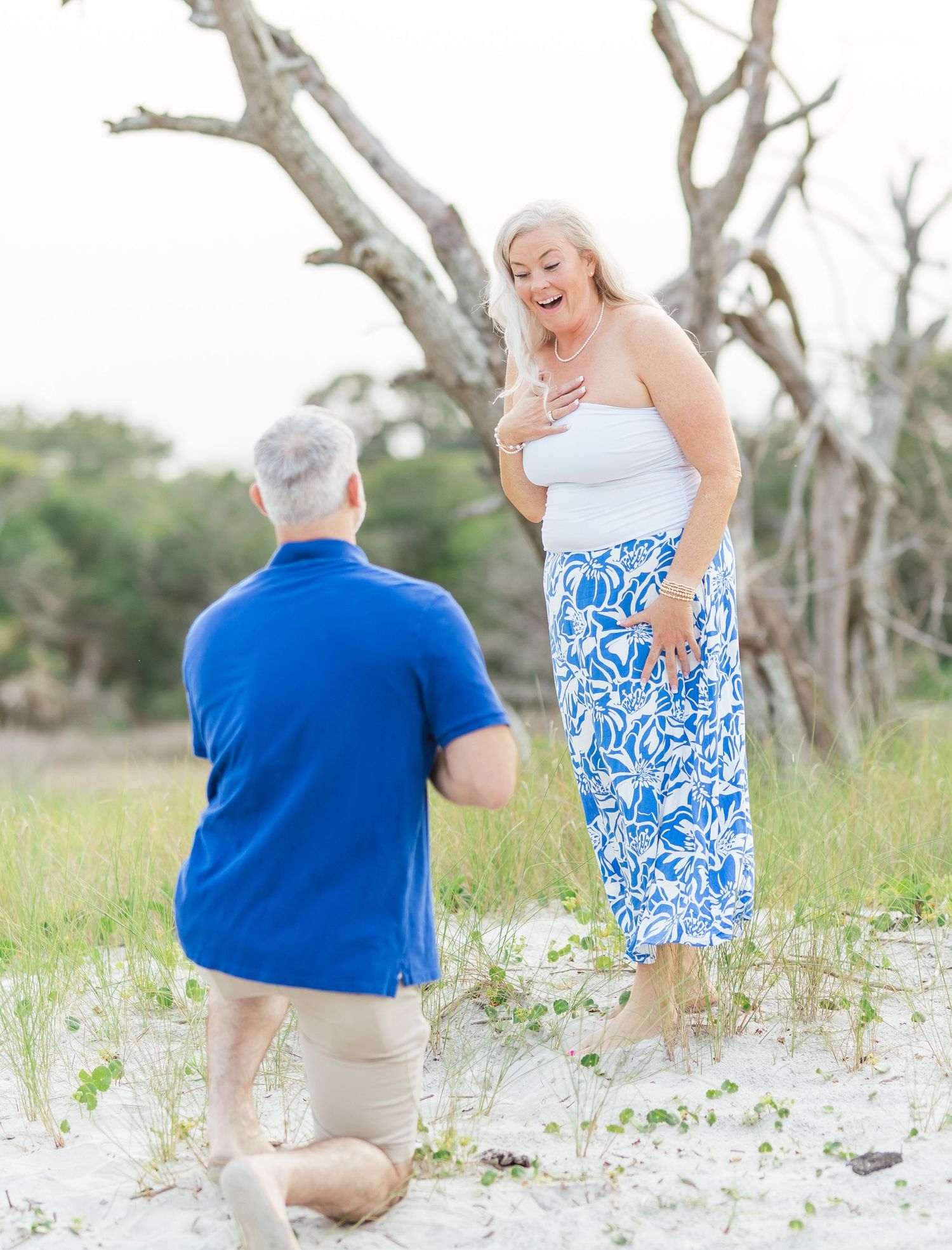 Couple shares joyful moments on a beach with weathered trees in the background.