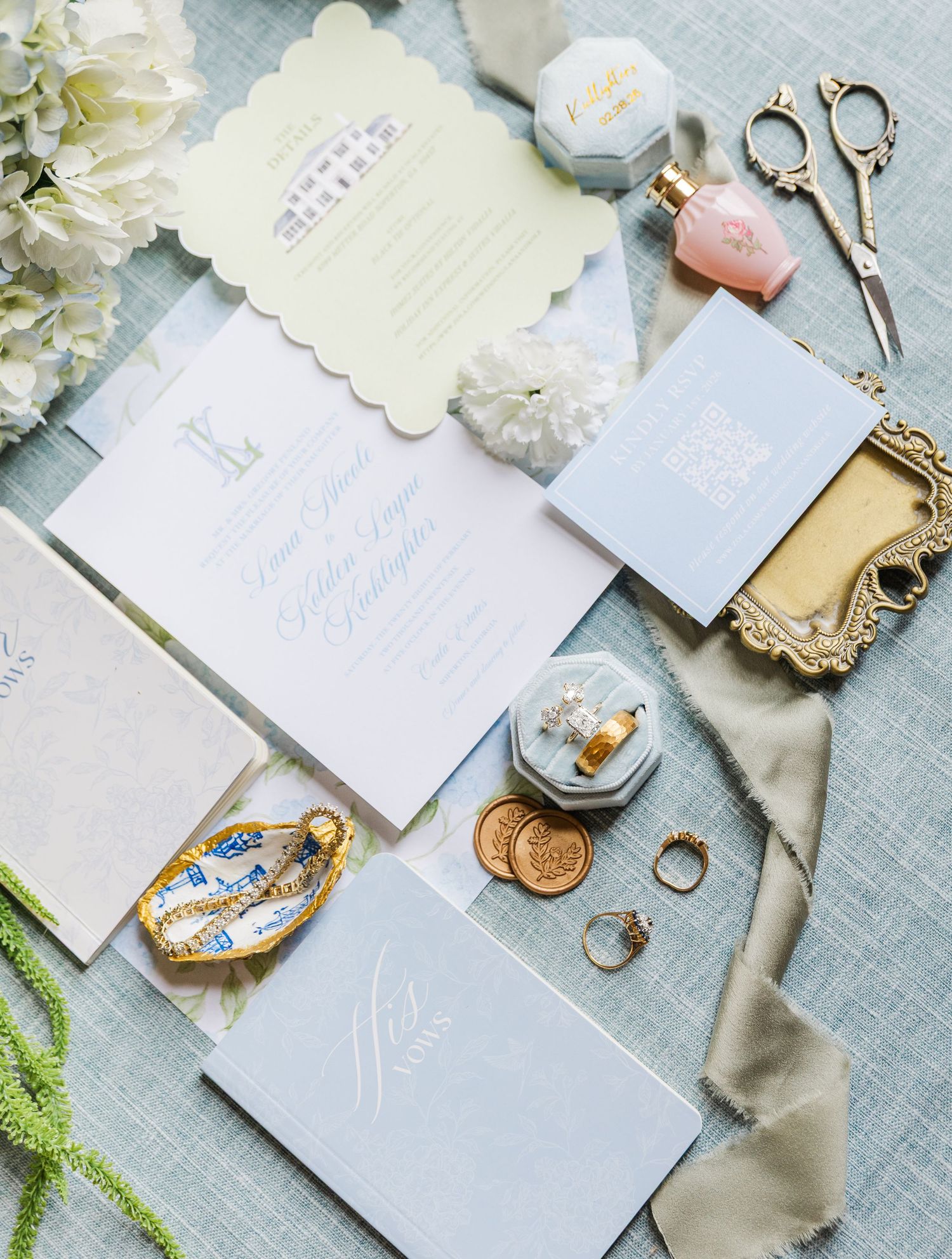 Blue and gold wedding invitation suite flat lay with hydrangeas, rings, perfume, and vintage scissors.