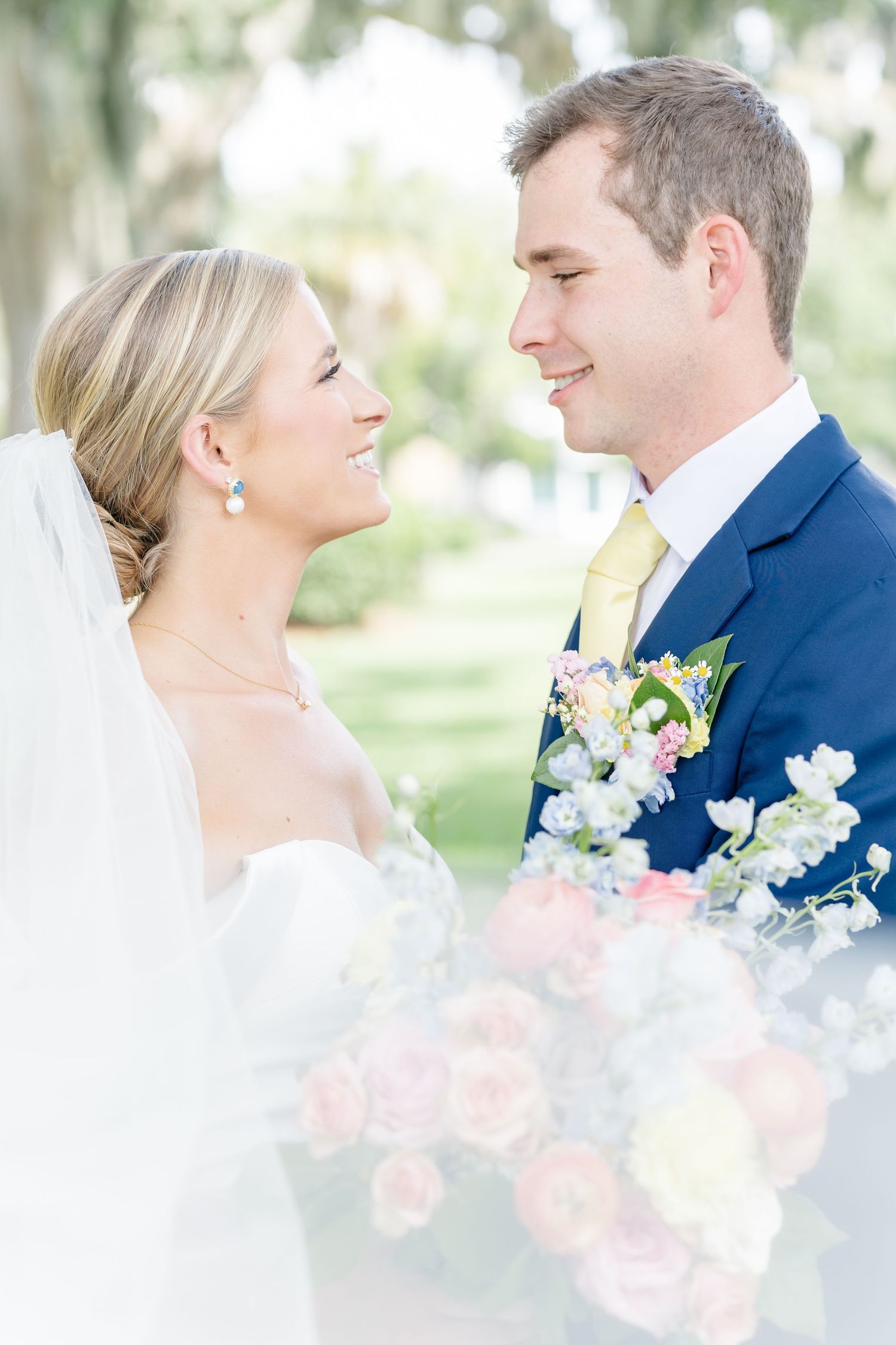 A romantic wedding couple shares intimate moments in a bright outdoor setting with pink and white floral bouquet details.