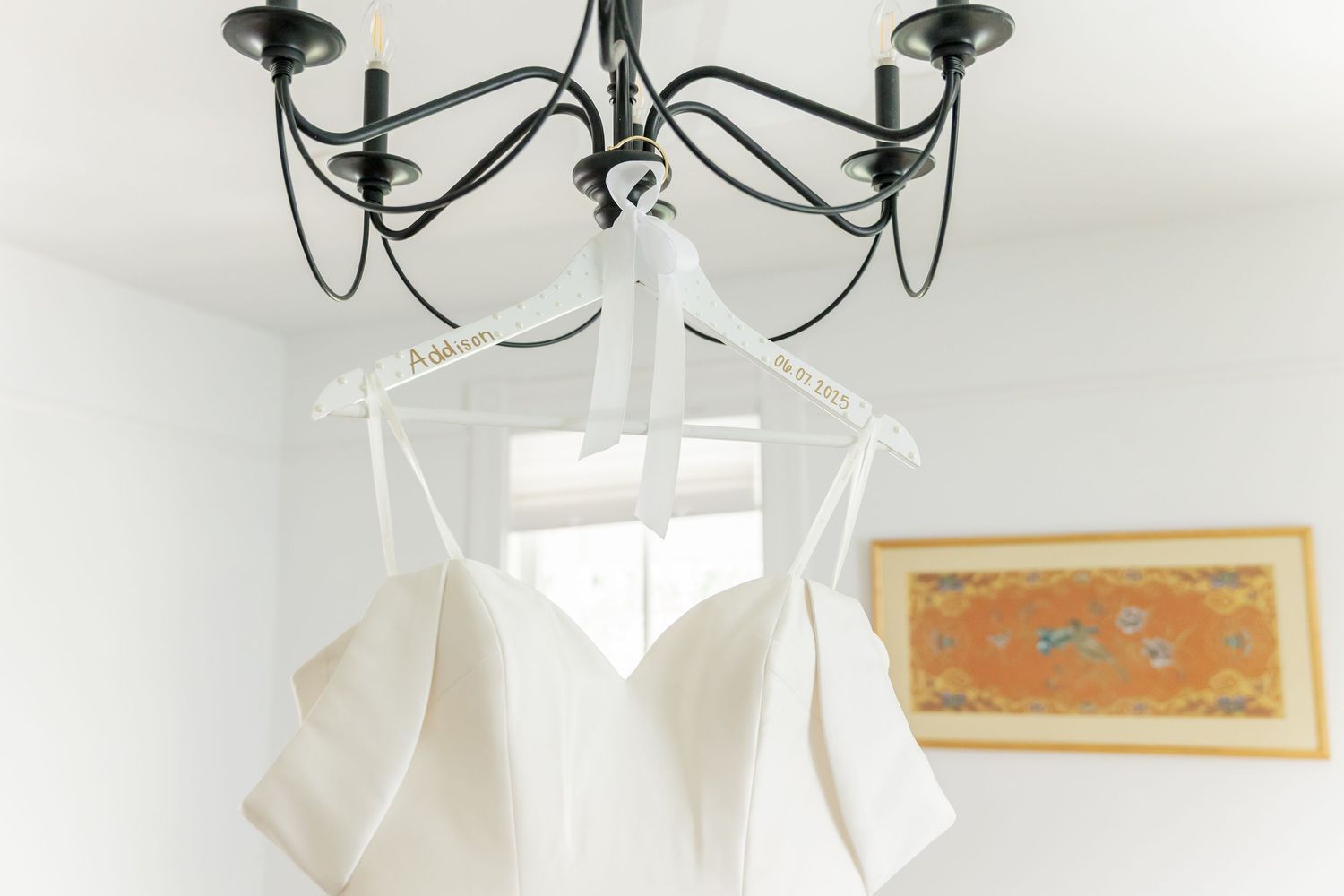 Elegant wedding details with delicate jewelry and paper elements arranged on a light surface under a chandelier.