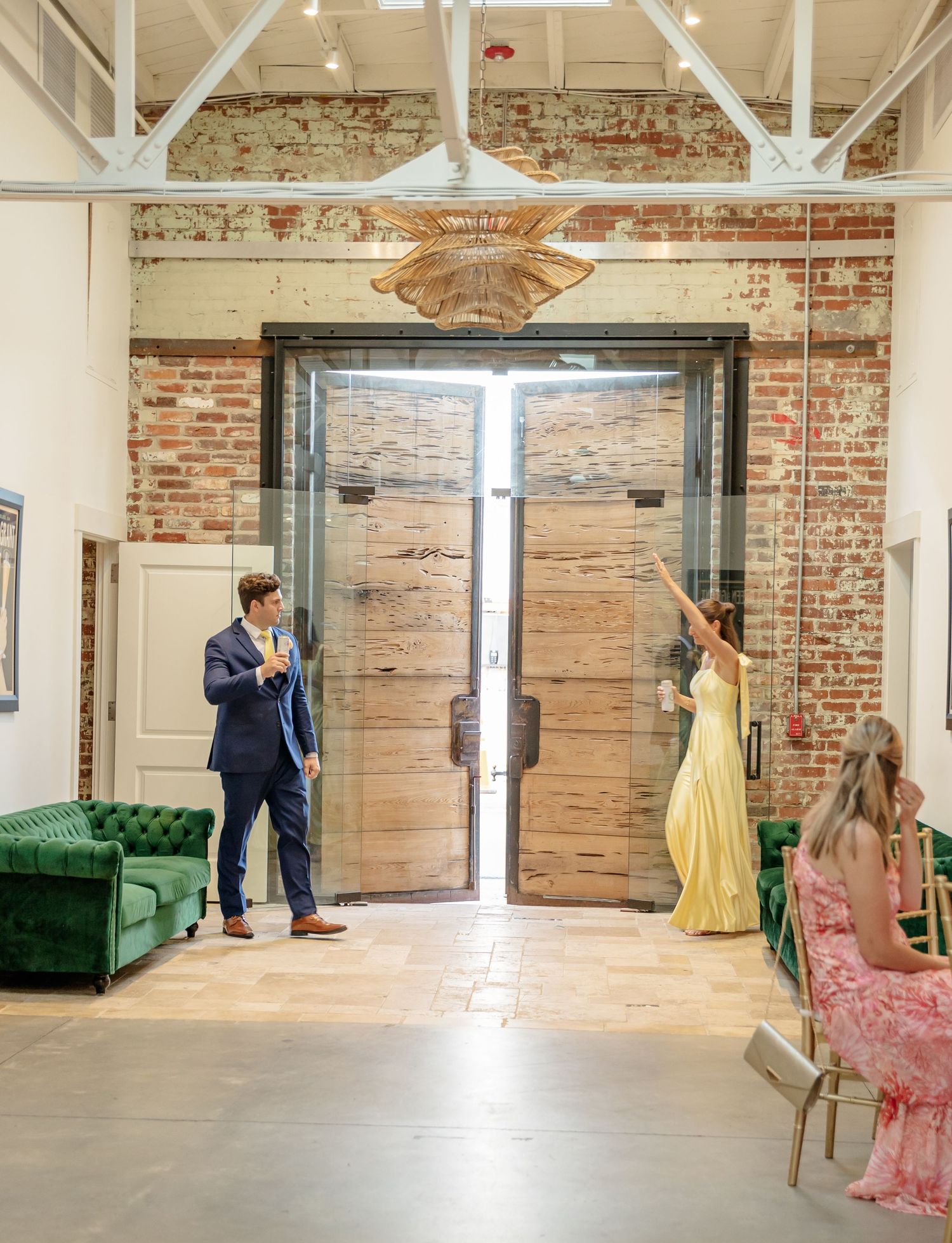 Elegant wedding venue interior featuring exposed brick walls, green velvet couch and large wooden doors.