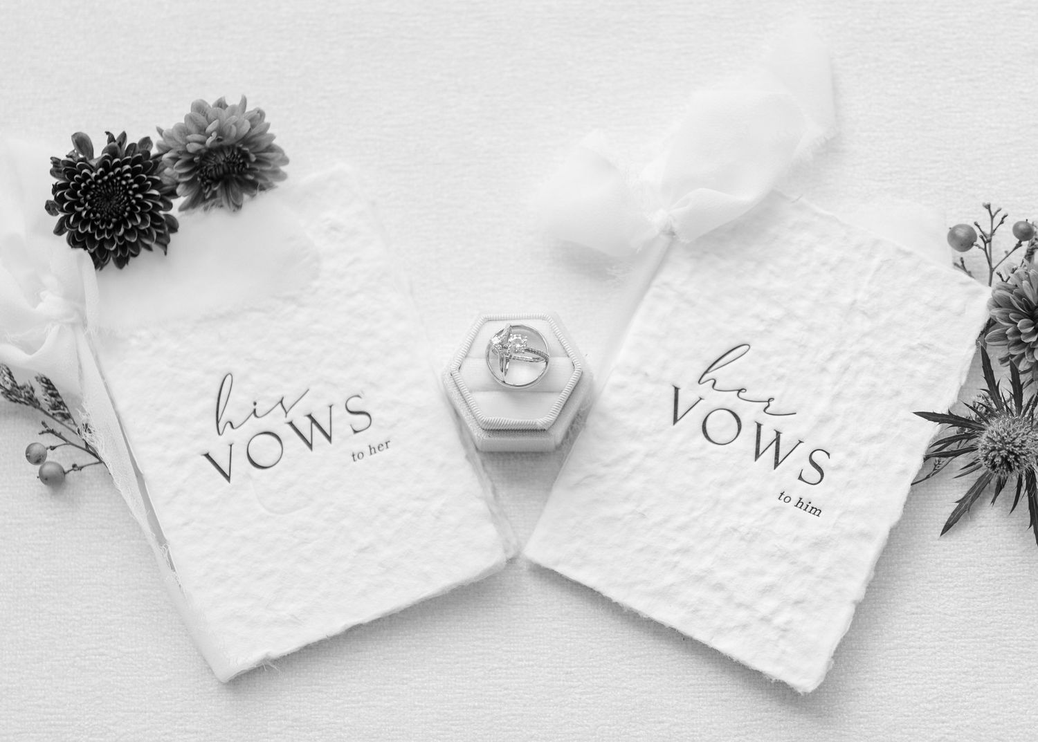 Elegant white wedding vow books and floral arrangements displayed on a light gray surface.