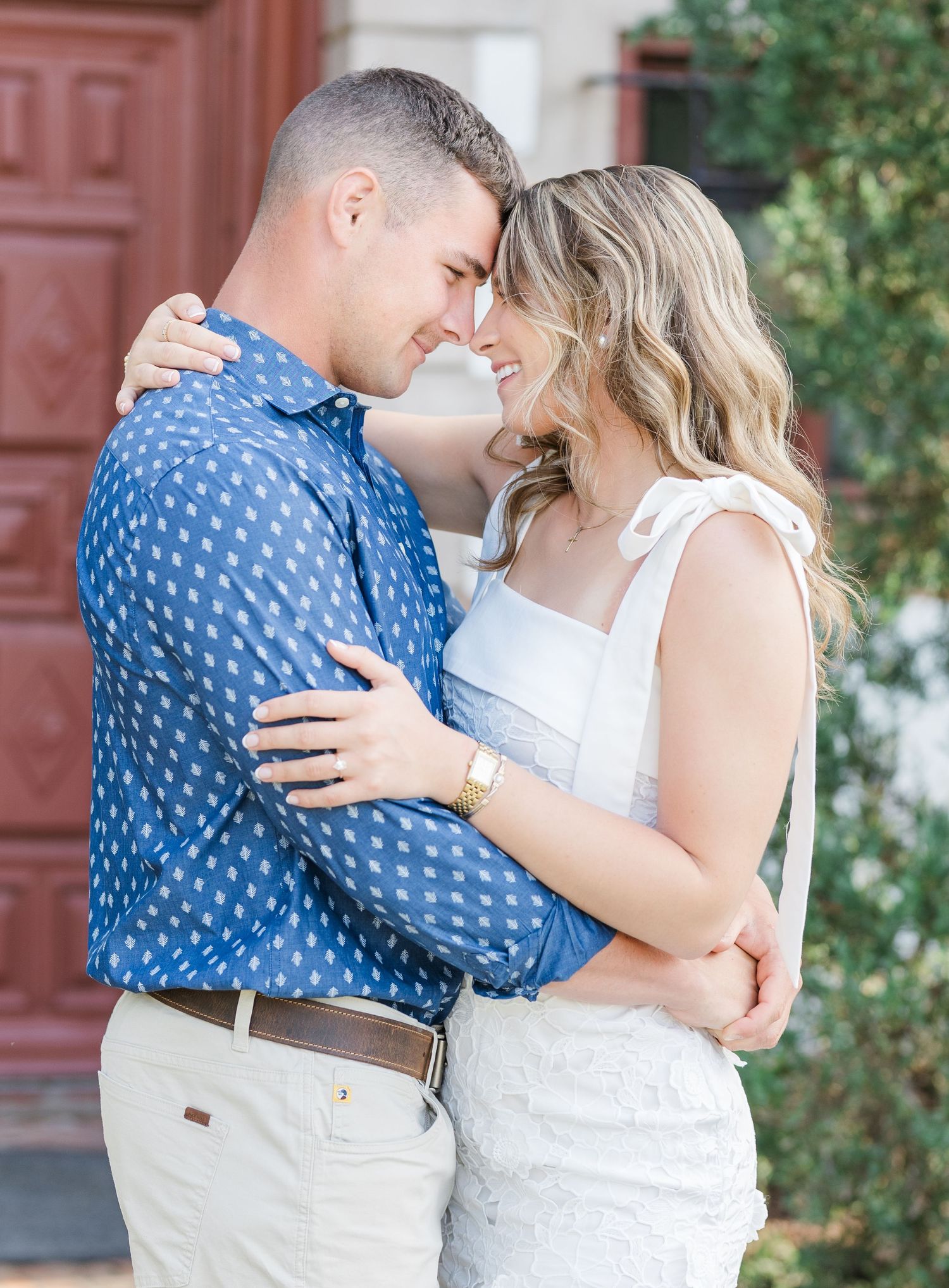 Romantic couple embracing and smiling at each other outdoors near a red door.