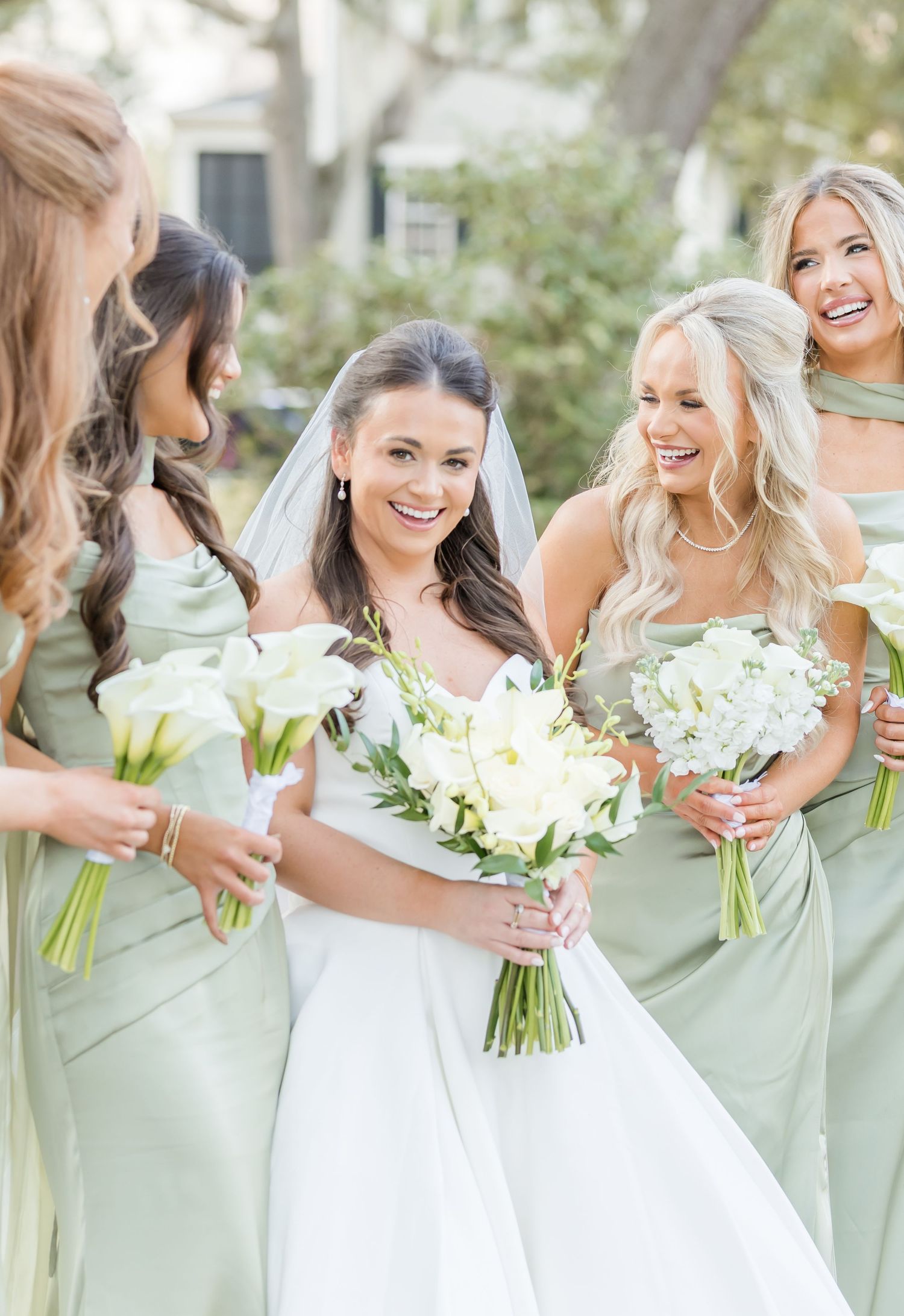 Smiling bride in white wedding gown surrounded by bridesmaids in mint green dresses with white bouquets.