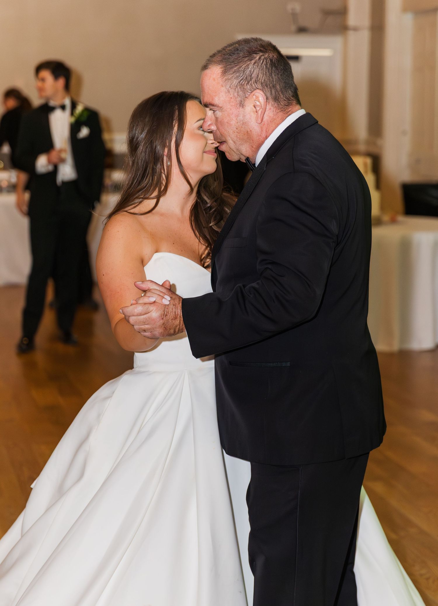 Bride and older man share an intimate first dance at wedding reception in elegant ballroom venue.