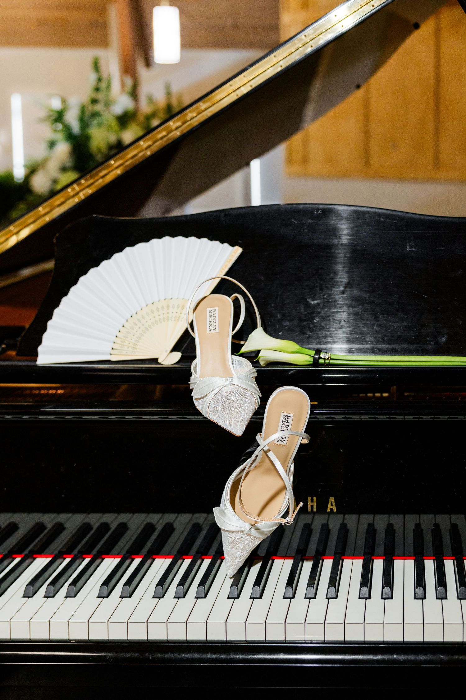 Bridal heels and white fan displayed on Yamaha grand piano keys with calla lily for wedding.