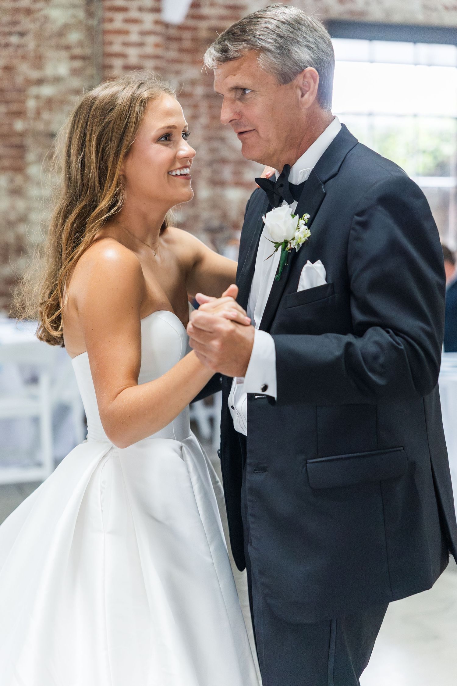 Bride shares joyful father-daughter dance at wedding reception in rustic brick venue.