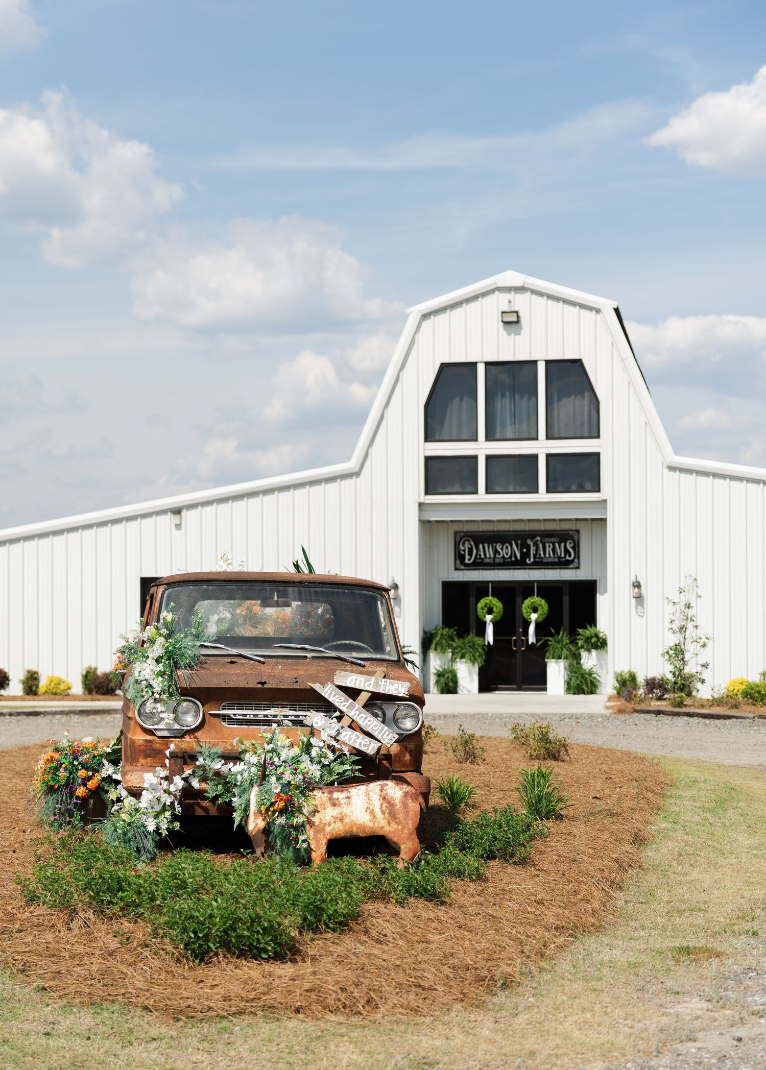 White barn wedding venue Dawson Farms with vintage rusty truck decorated with flowers at entrance.