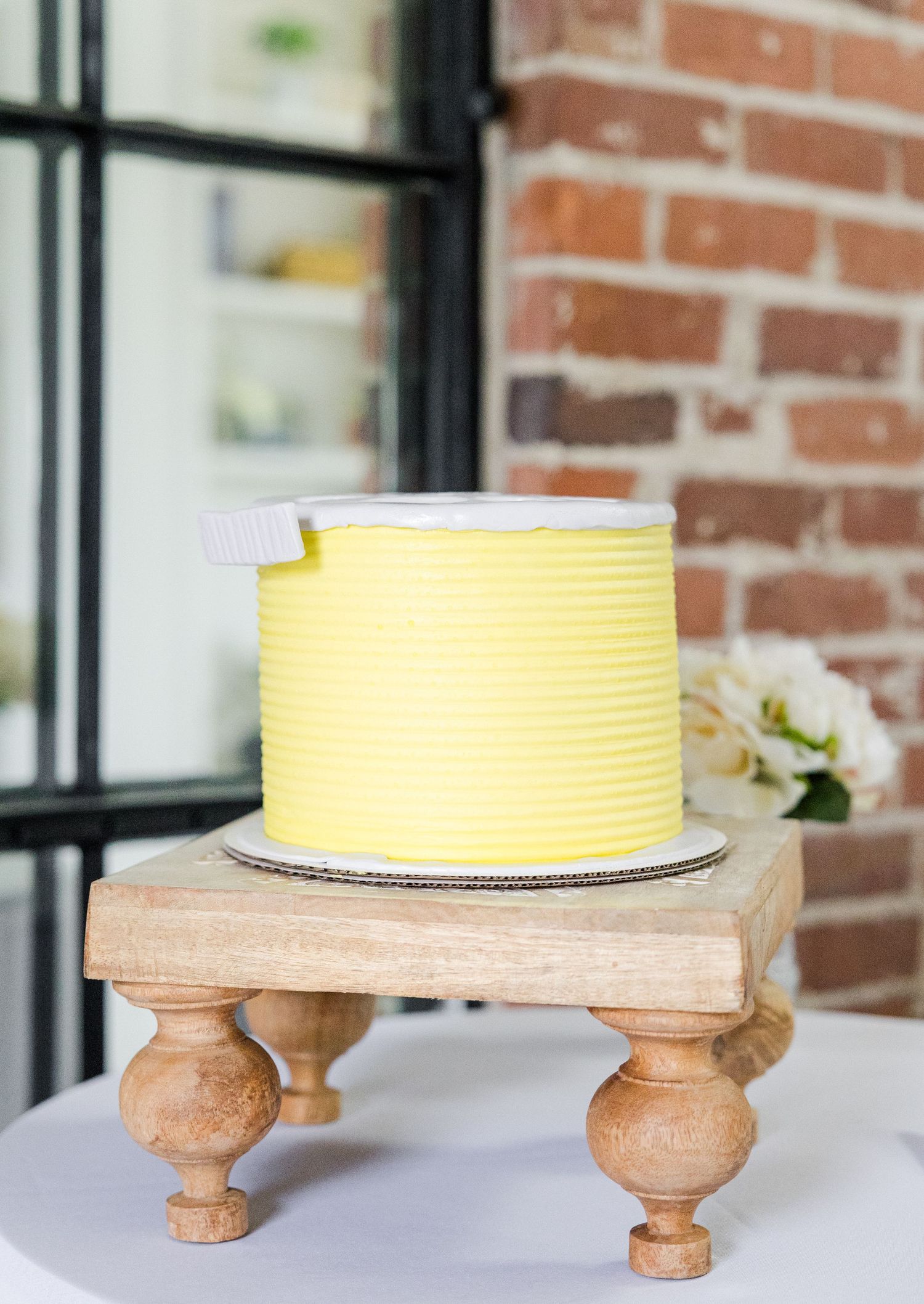 Yellow ribbed fondant cake on a wooden cake stand with brick wall background.