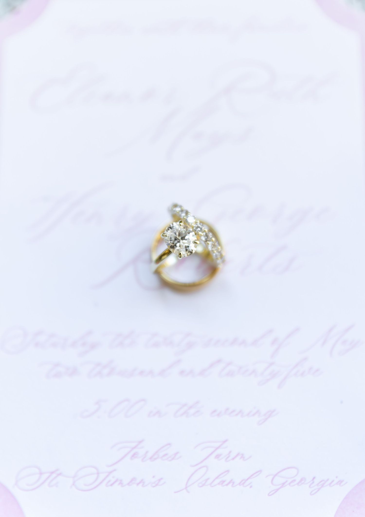 Two shiny engagement rings with diamonds sit side by side against a soft pink blurred background.