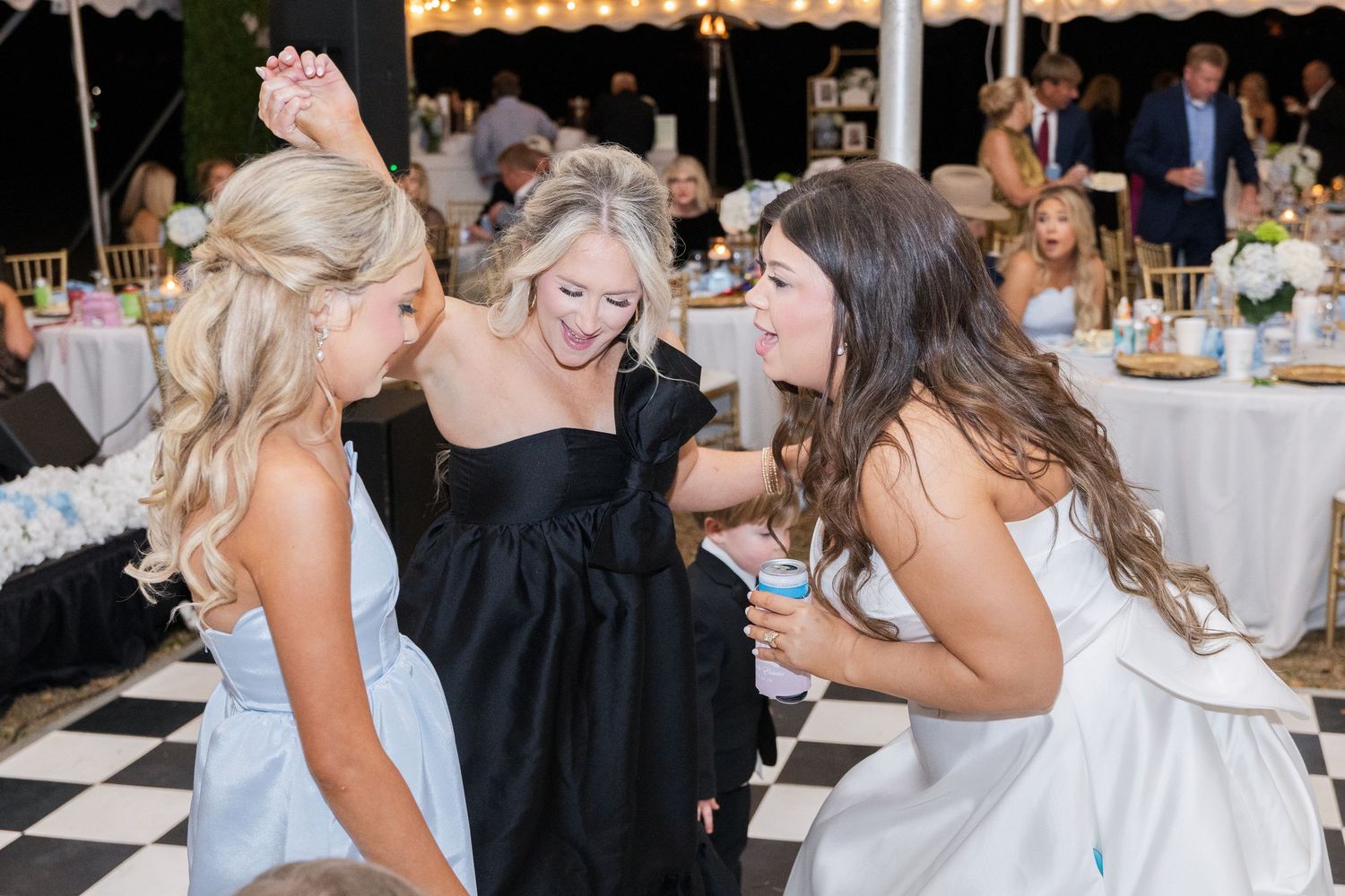 Bride and guests dancing and celebrating together on a black and white checkered dance floor at reception.