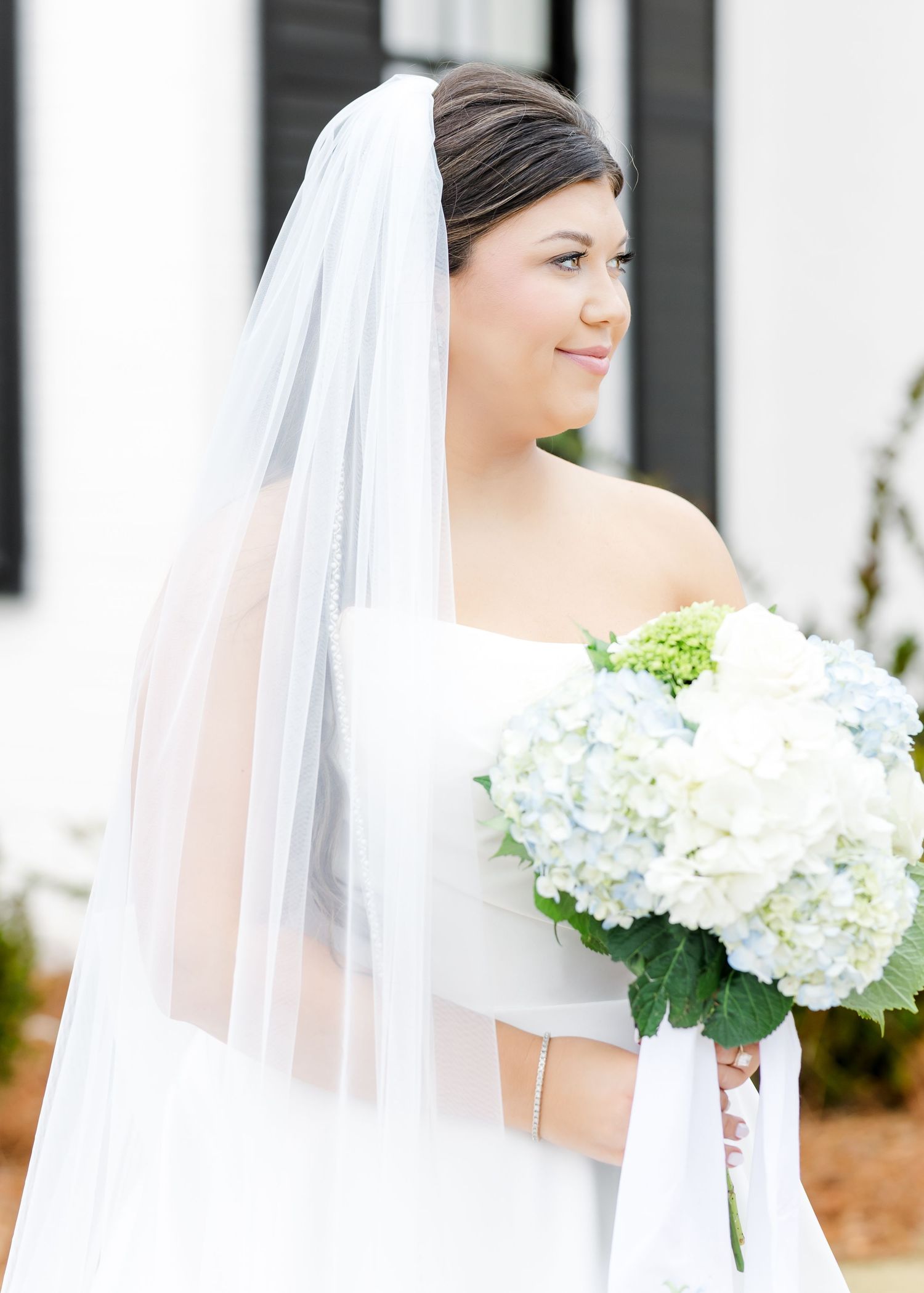 Bride wearing a white strapless gown and veil holding a blue and white hydrangea bouquet.