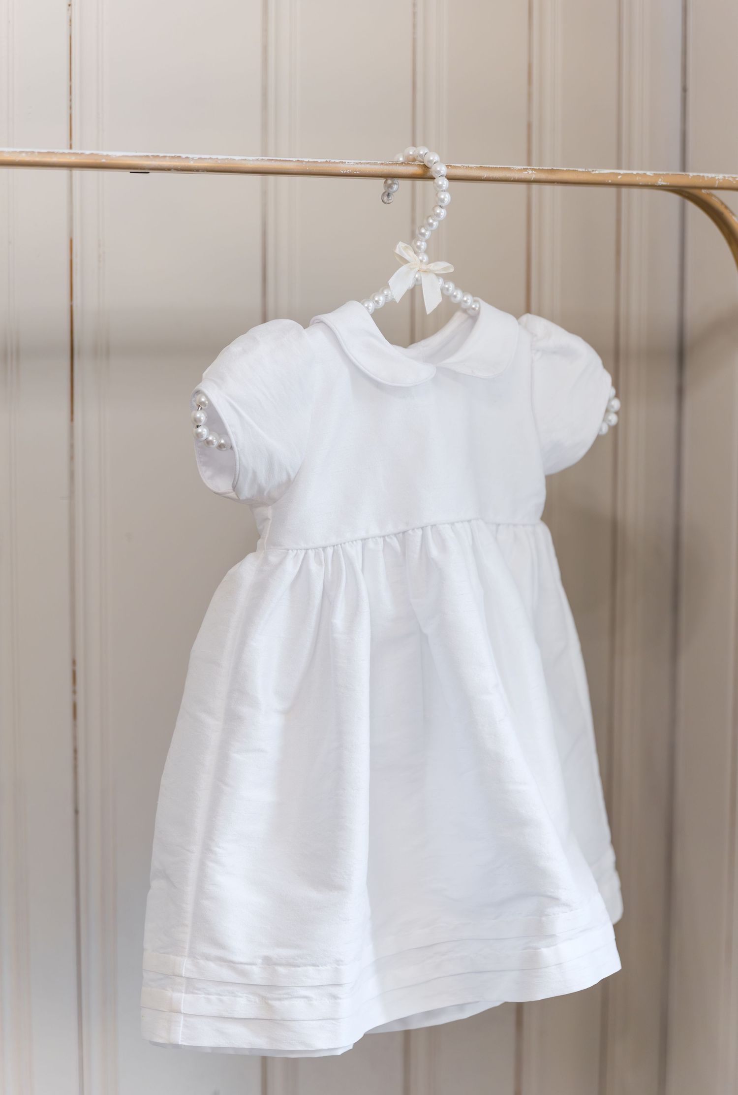 White baby girl dress with peter pan collar and puff sleeves hanging on a wooden hanger.