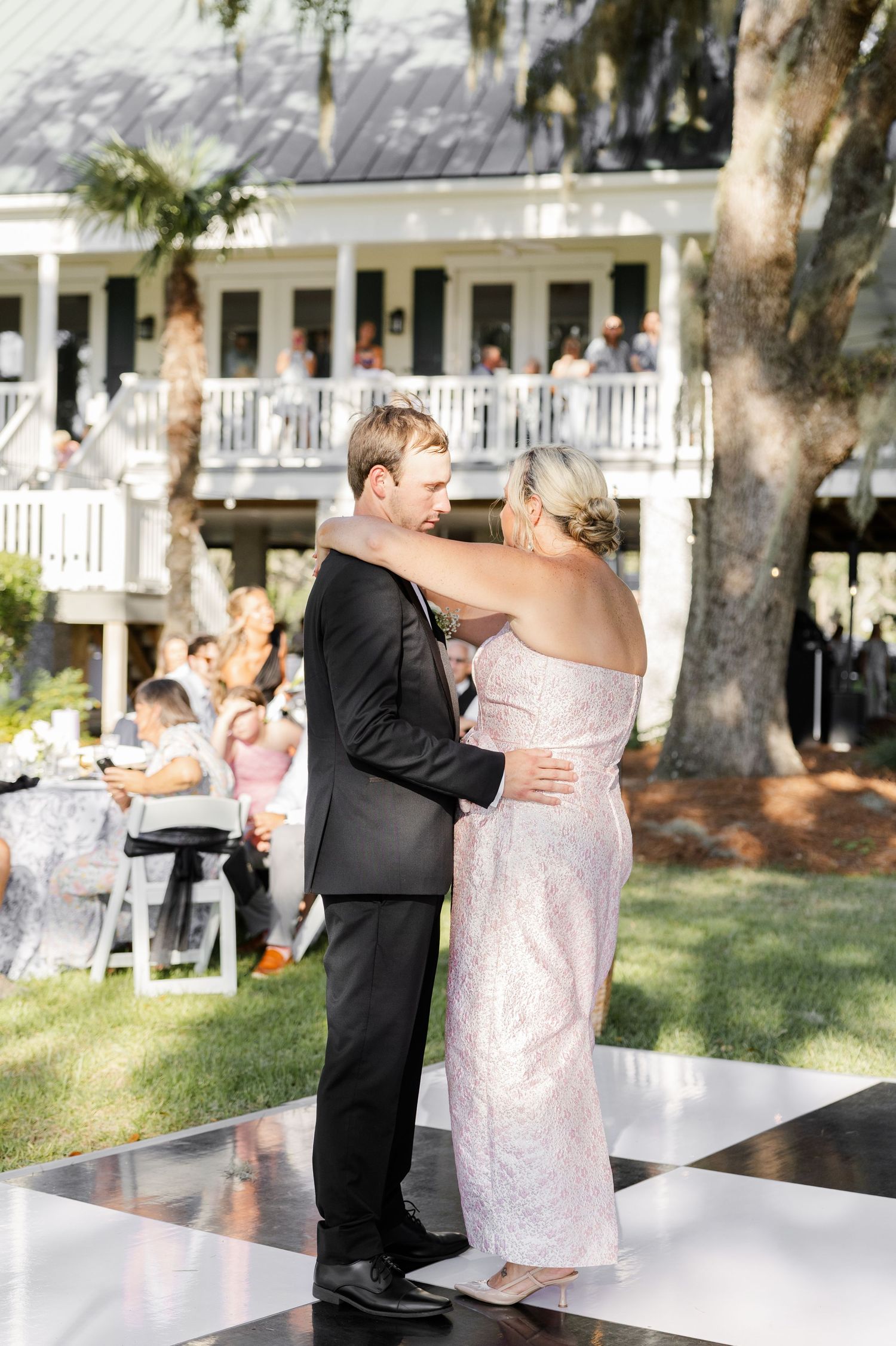 Groom dances with mother in pink sequin gown on checkered floor at elegant outdoor wedding reception.