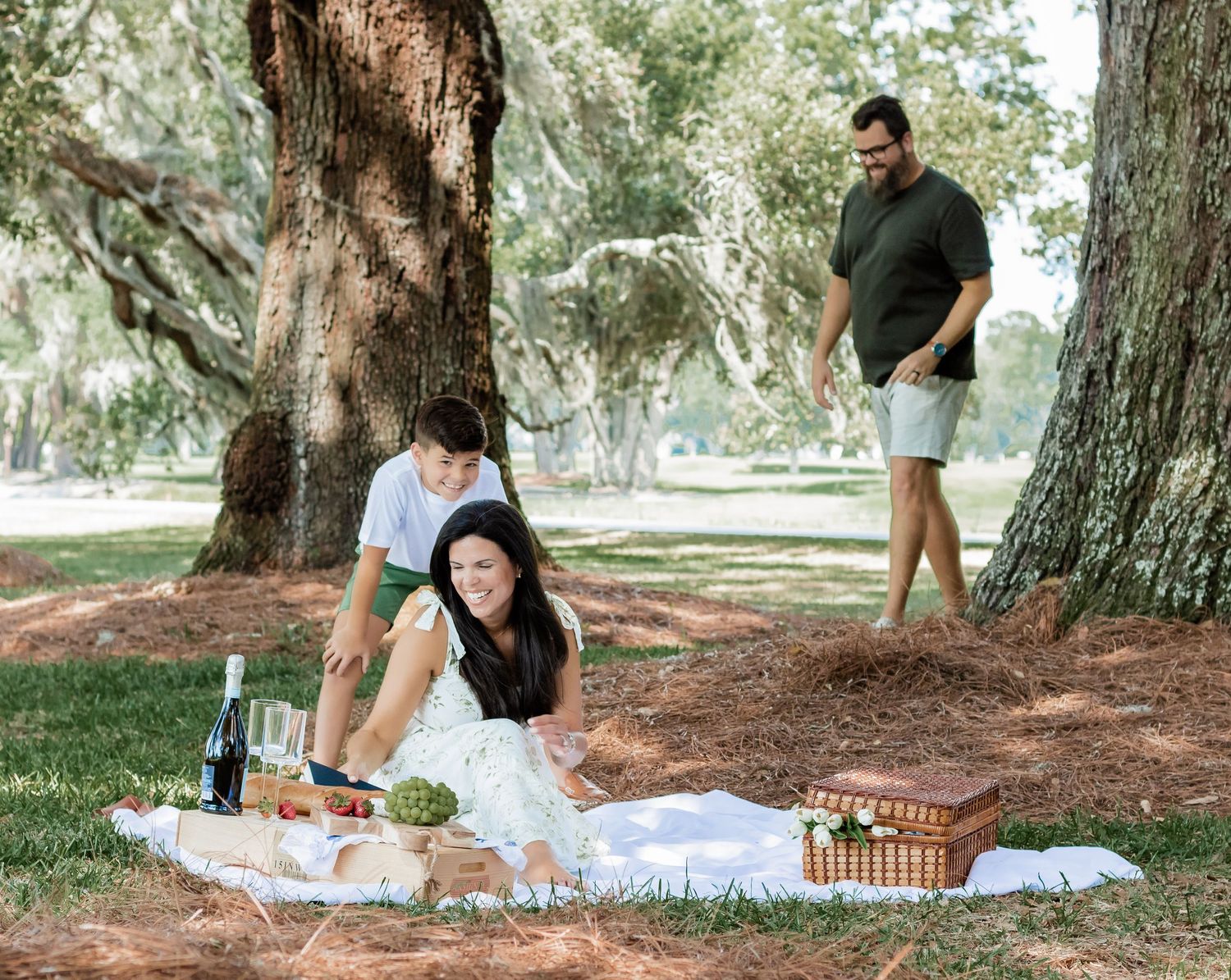 Family enjoying an outdoor picnic while playing around massive oak trees.