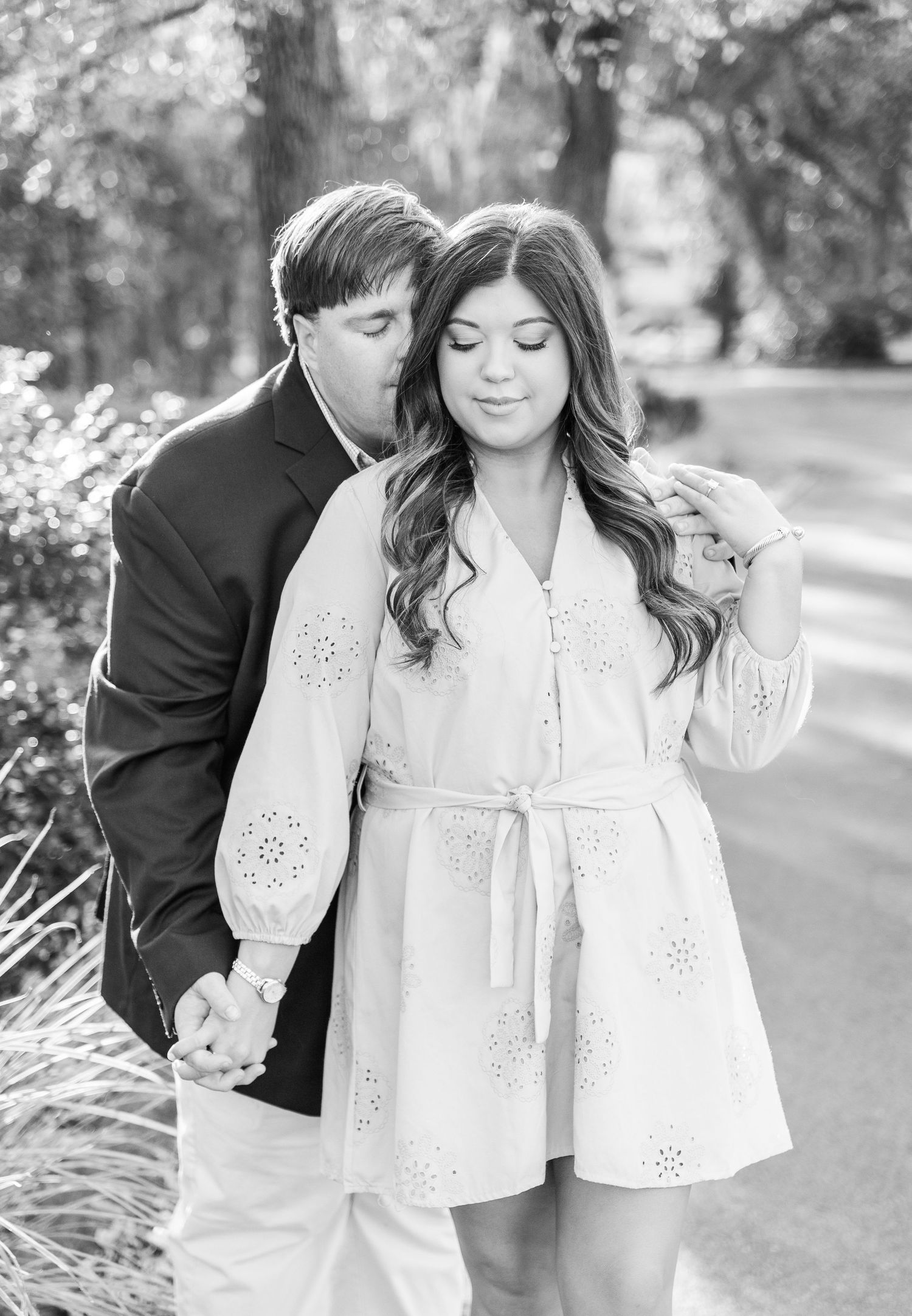 A romantic black and white portrait of a couple embracing in a garden setting.