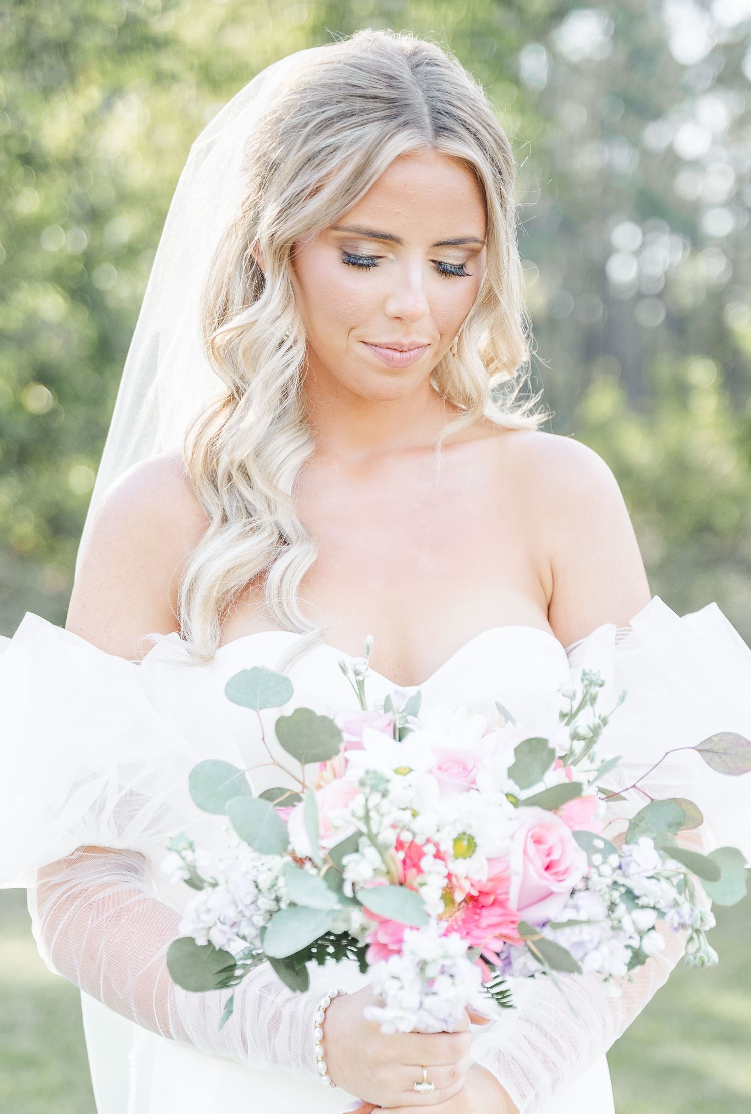 Soft portrait of bride with cascading waves and delicate makeup holding pink and white bouquet.
