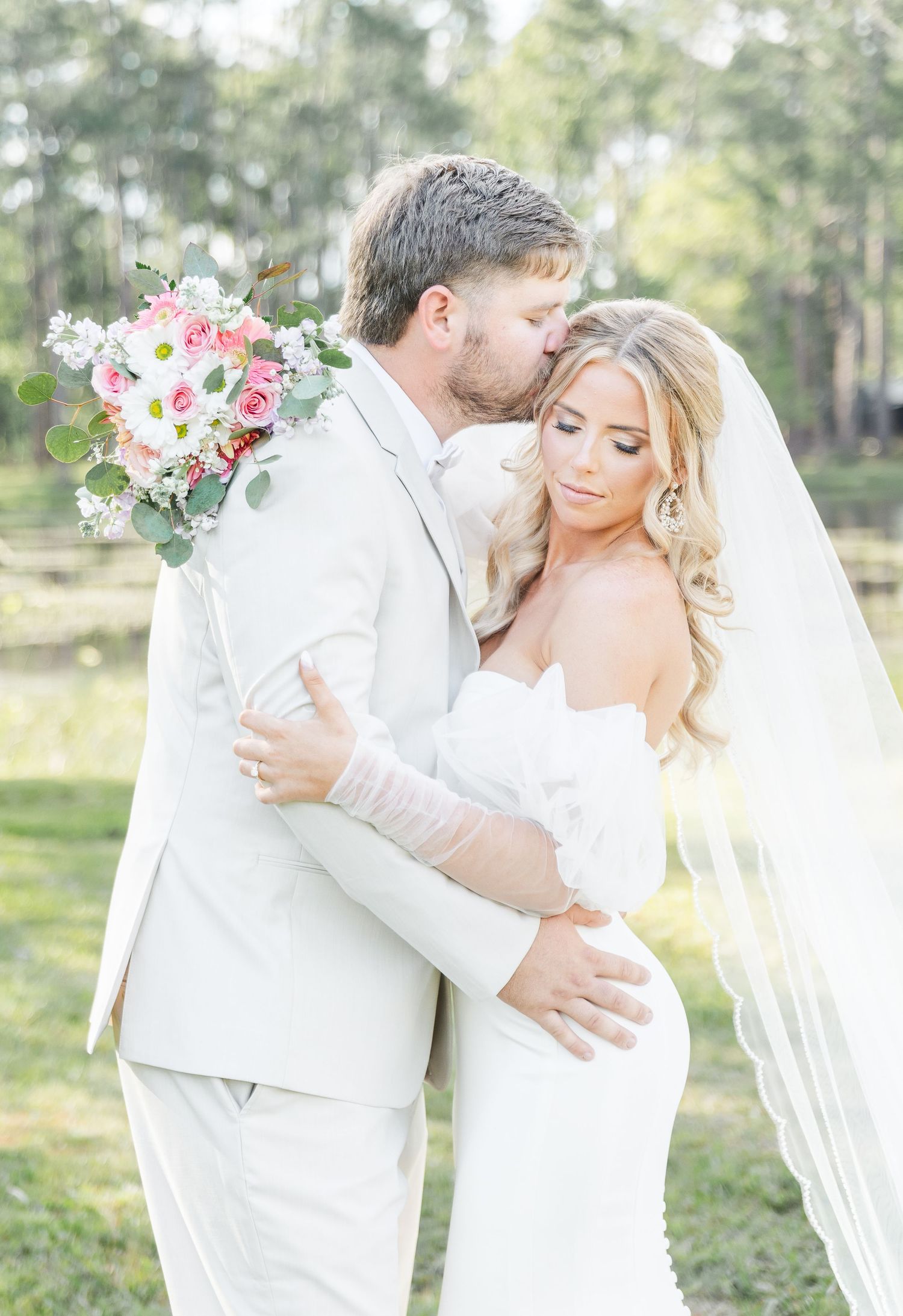 Romantic wedding portrait with bride and groom embracing in a sunlit outdoor setting.